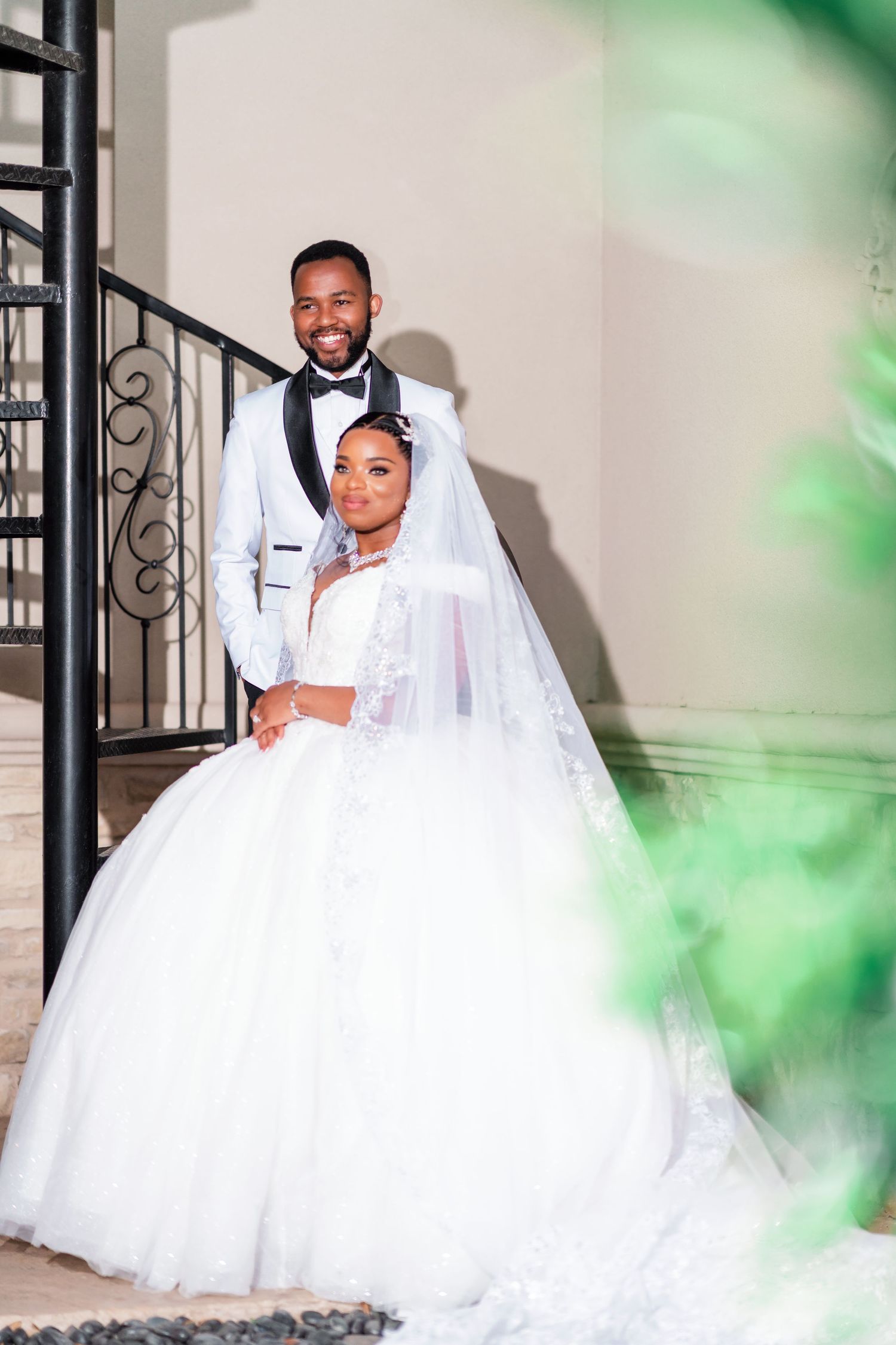 A romantic wedding photoshoot featuring a couple in white attire posing against a soft green background.