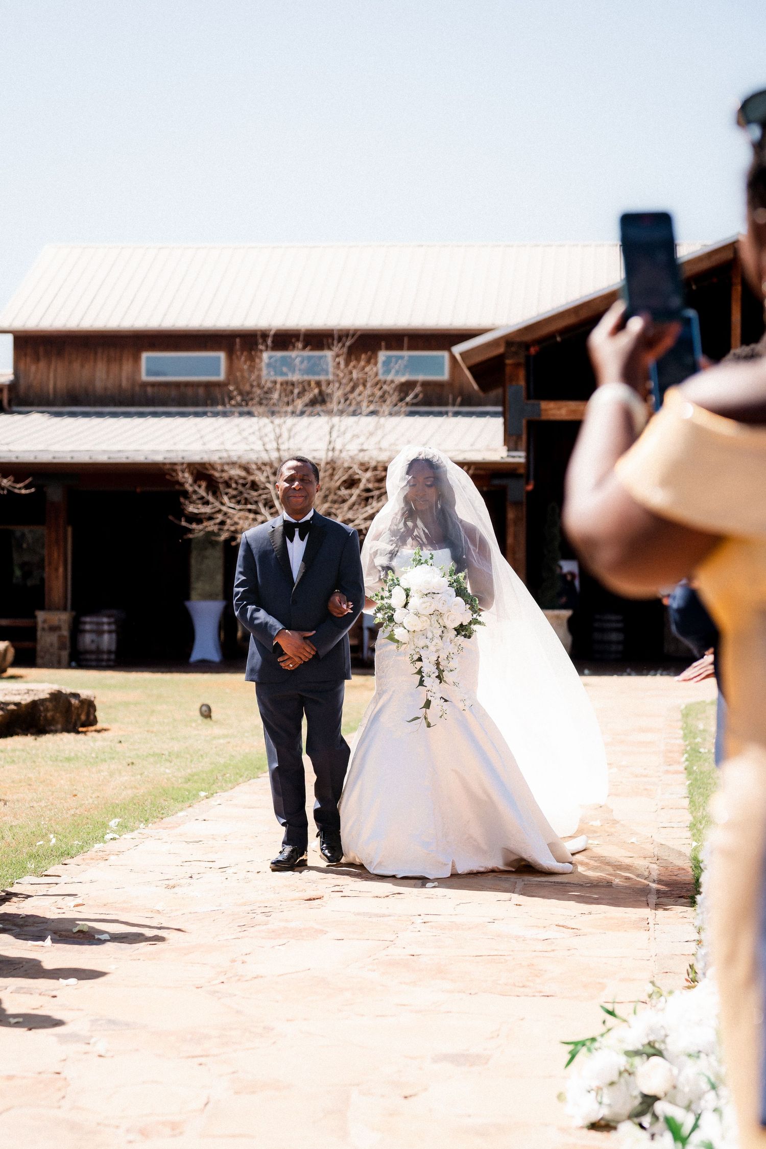 Wedding party poses on a stone pathway outside a rustic venue.
