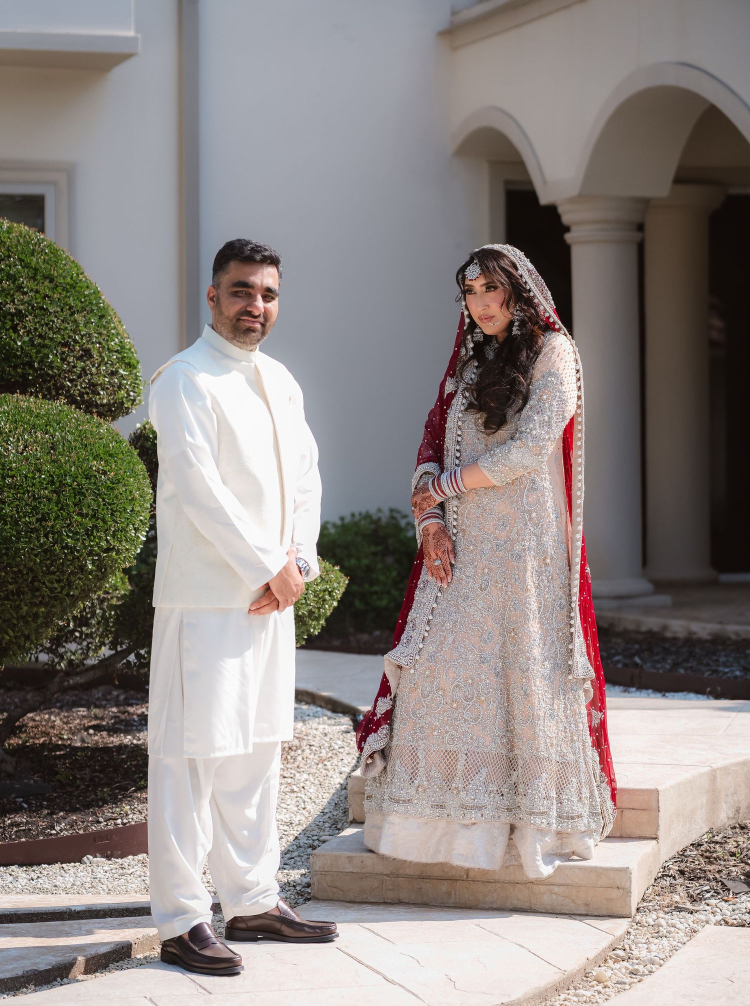 Wedding couple in traditional attire posing outside a white columned building.