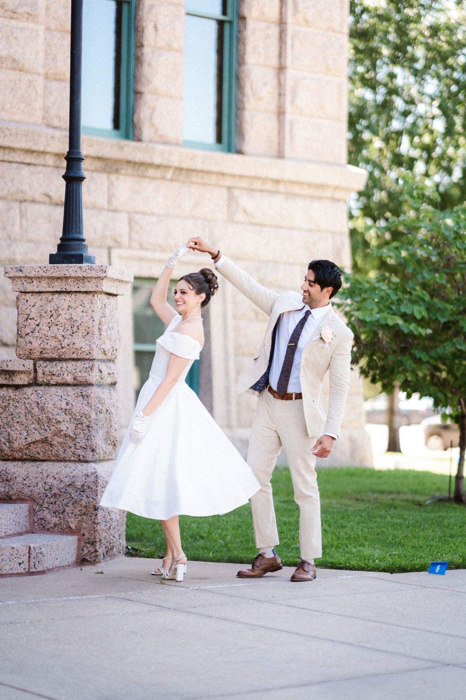 A couple in white and beige attire dances playfully on stone steps outdoors.
