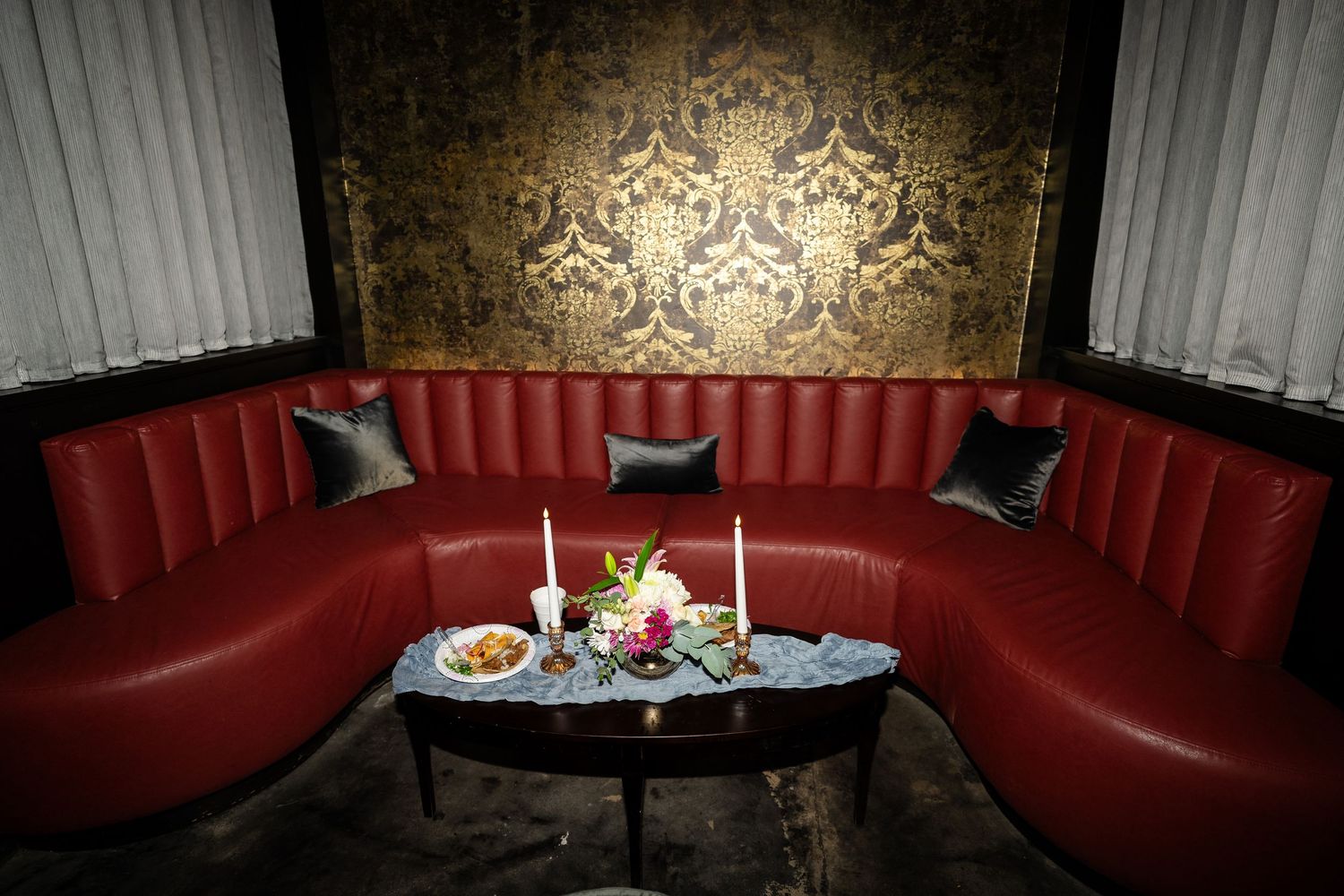 Luxurious curved red leather booth with ornate wallpaper and romantic candlelit table setting for two.