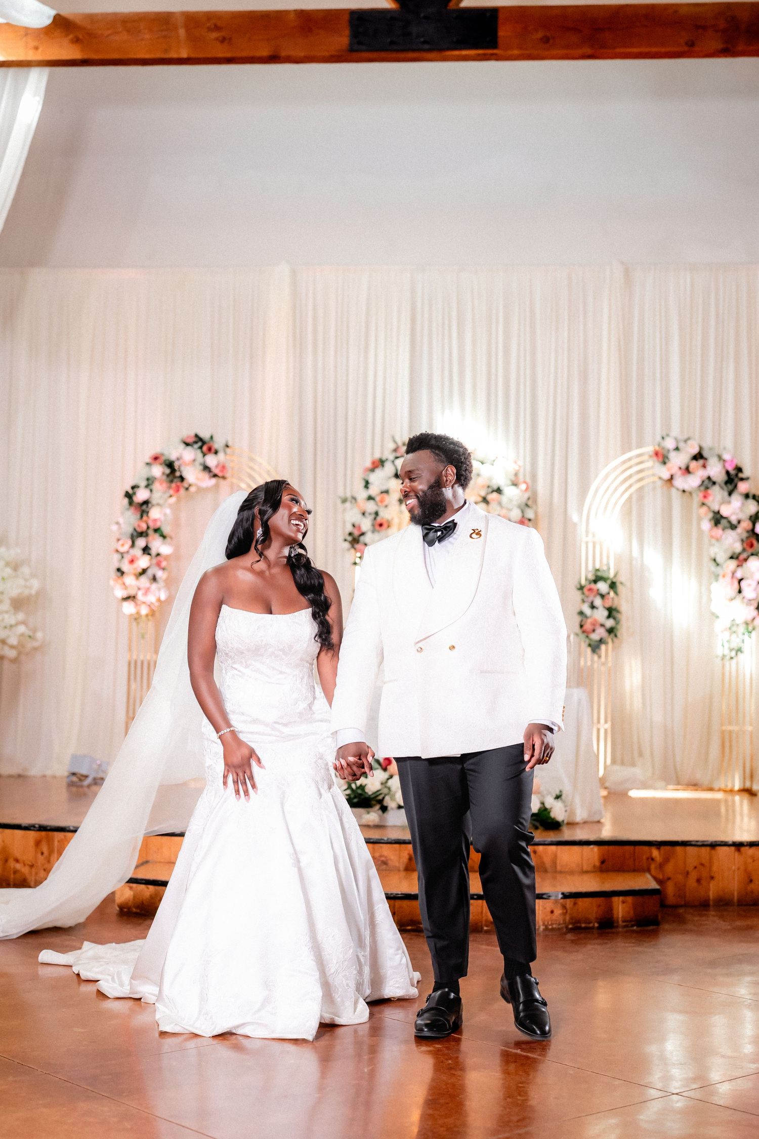 A couple poses under floral arches in an elegantly decorated rustic wedding venue.
