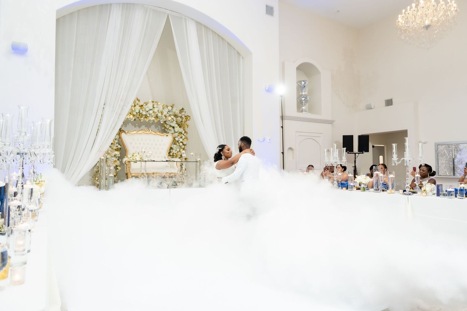 All-white wedding reception venue with flowing drapes, chandeliers and elegant decor throughout the space.