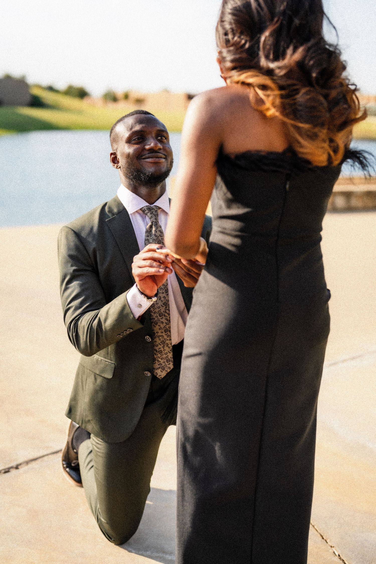 Romantic proposal moment captured by waterfront with sunset lighting.