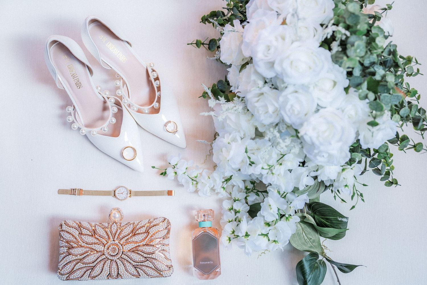 Elegant bridal accessories including rose gold jewelry and white floral arrangements on pale pink background.