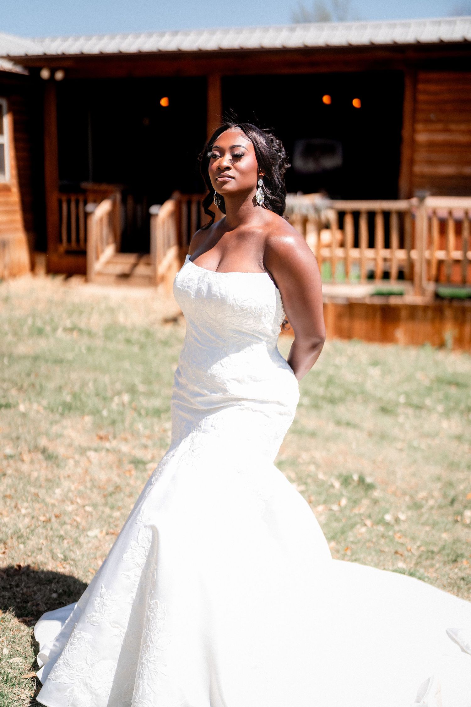 A bride poses in a stunning white mermaid wedding gown outside a rustic wooden cabin.