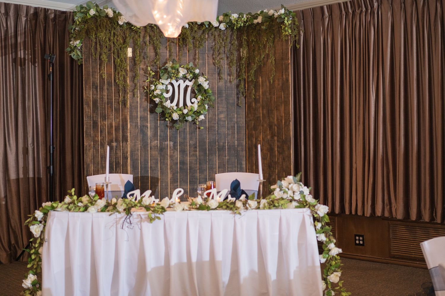 Wedding reception venue with elegant brown draping and floral decor along the head table.