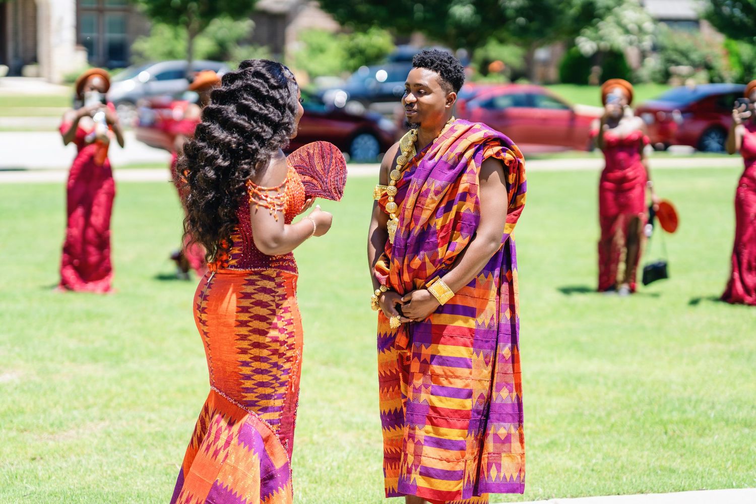 A gathering of people in colorful traditional African-inspired dresses and headwraps stand together outdoors.