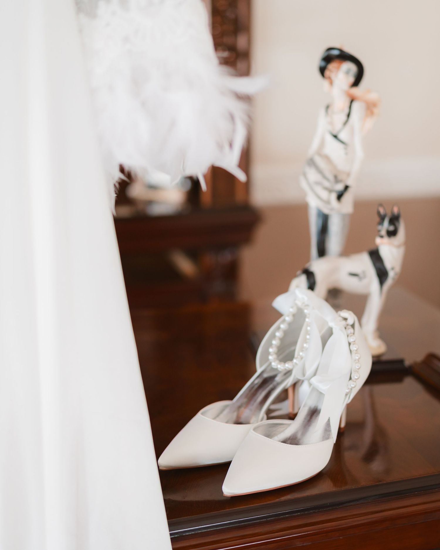 White bridal shoes and wedding dress details displayed on dark wooden furniture.