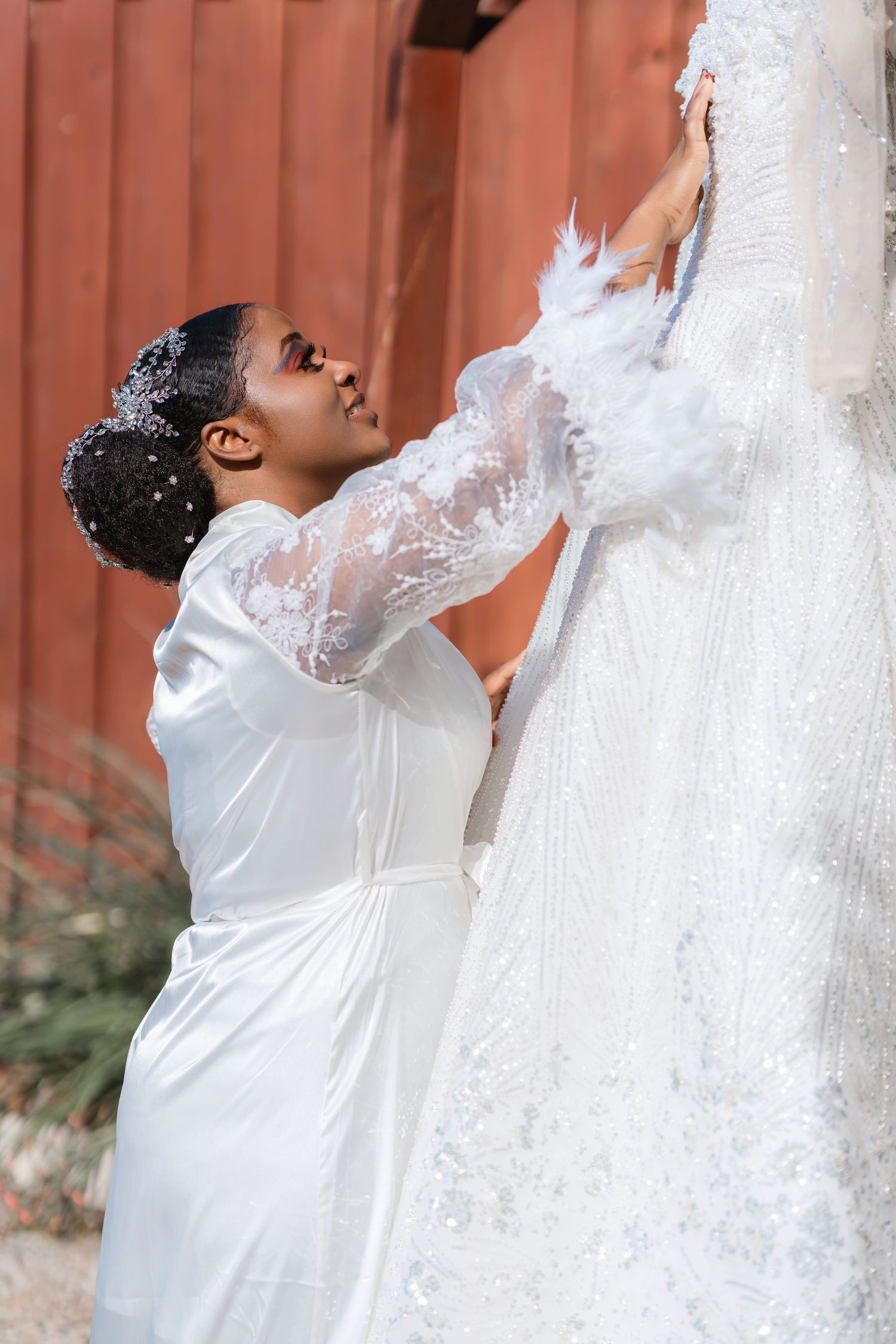 Emotional pre-wedding moment as bride reaches up to touch her hanging wedding gown.