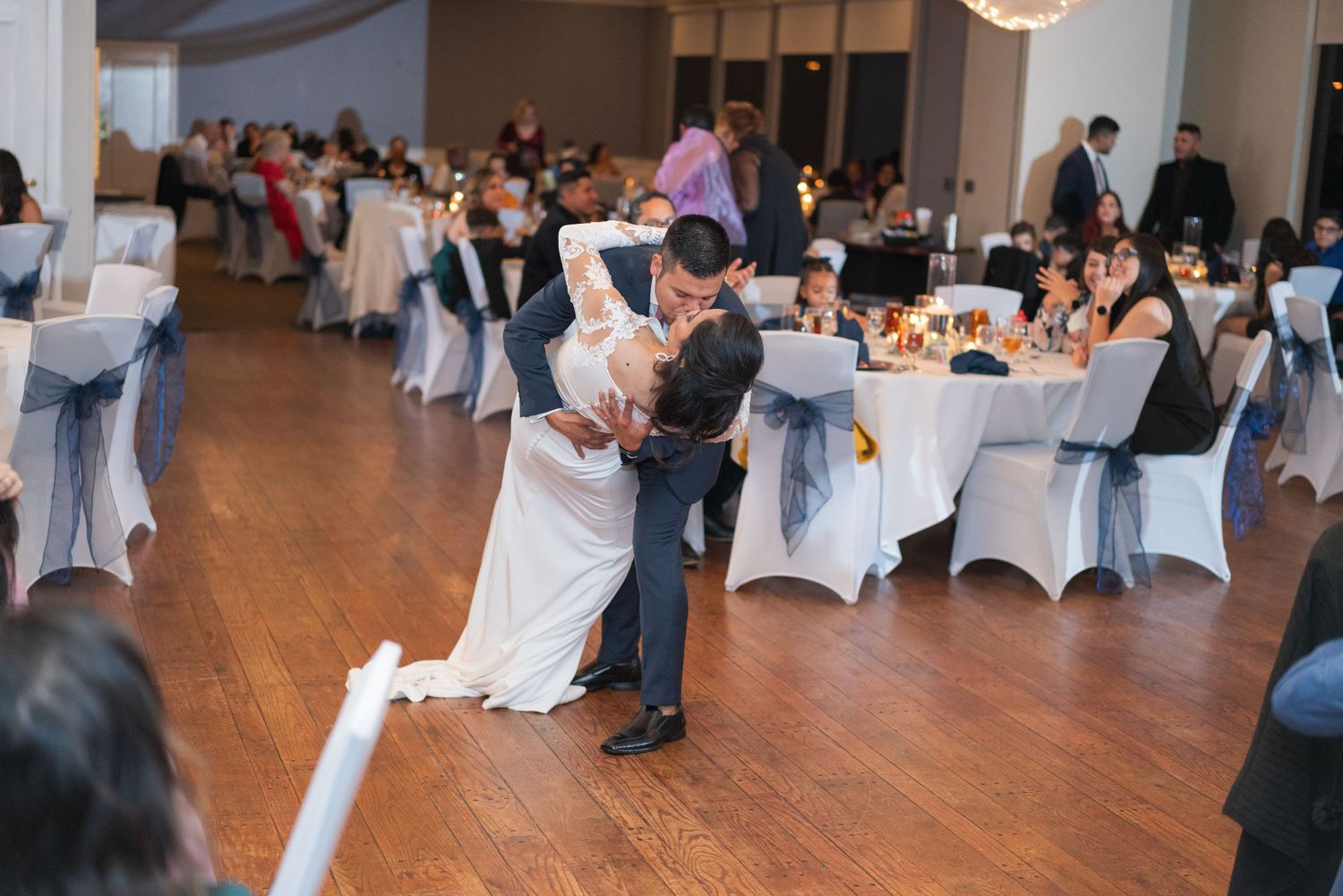 Wedding reception venue with white-covered chairs and guests celebrating on the dance floor.