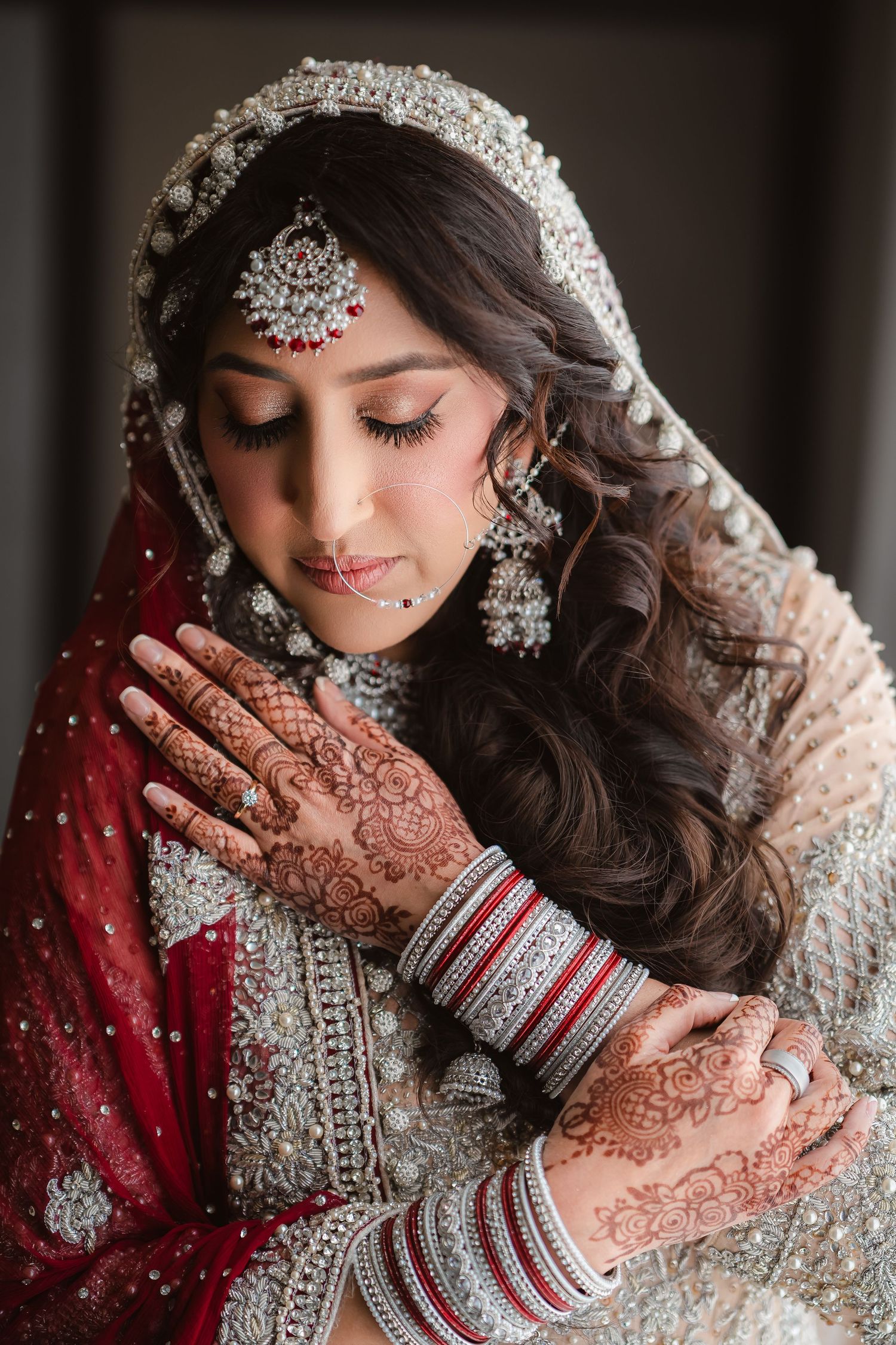 A close-up shot of intricate bridal henna designs and bangles with a red and silver embellished outfit.