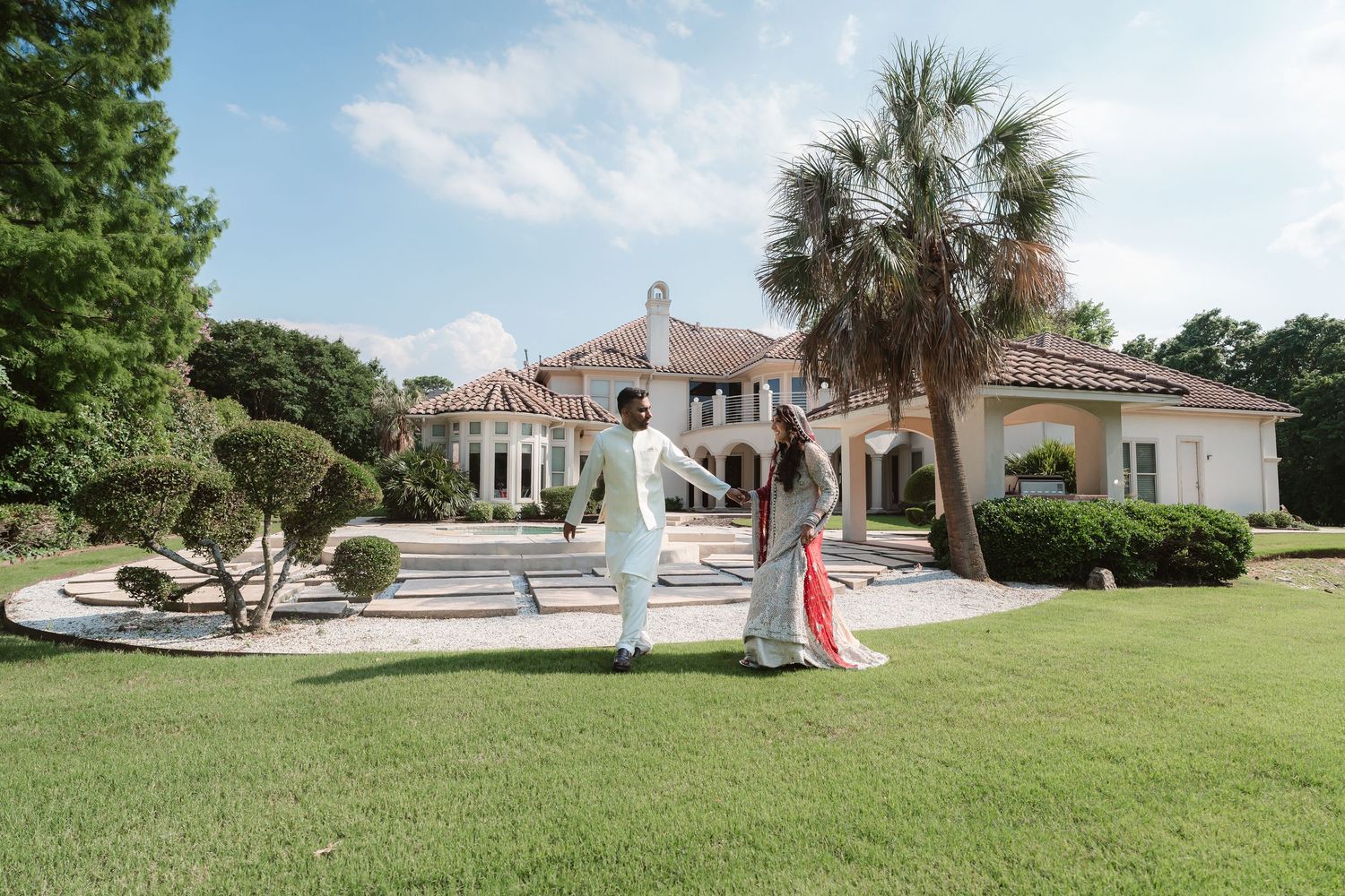 A panoramic view of a wedding ceremony setup on a lush green lawn with palm trees and Spanish architecture.