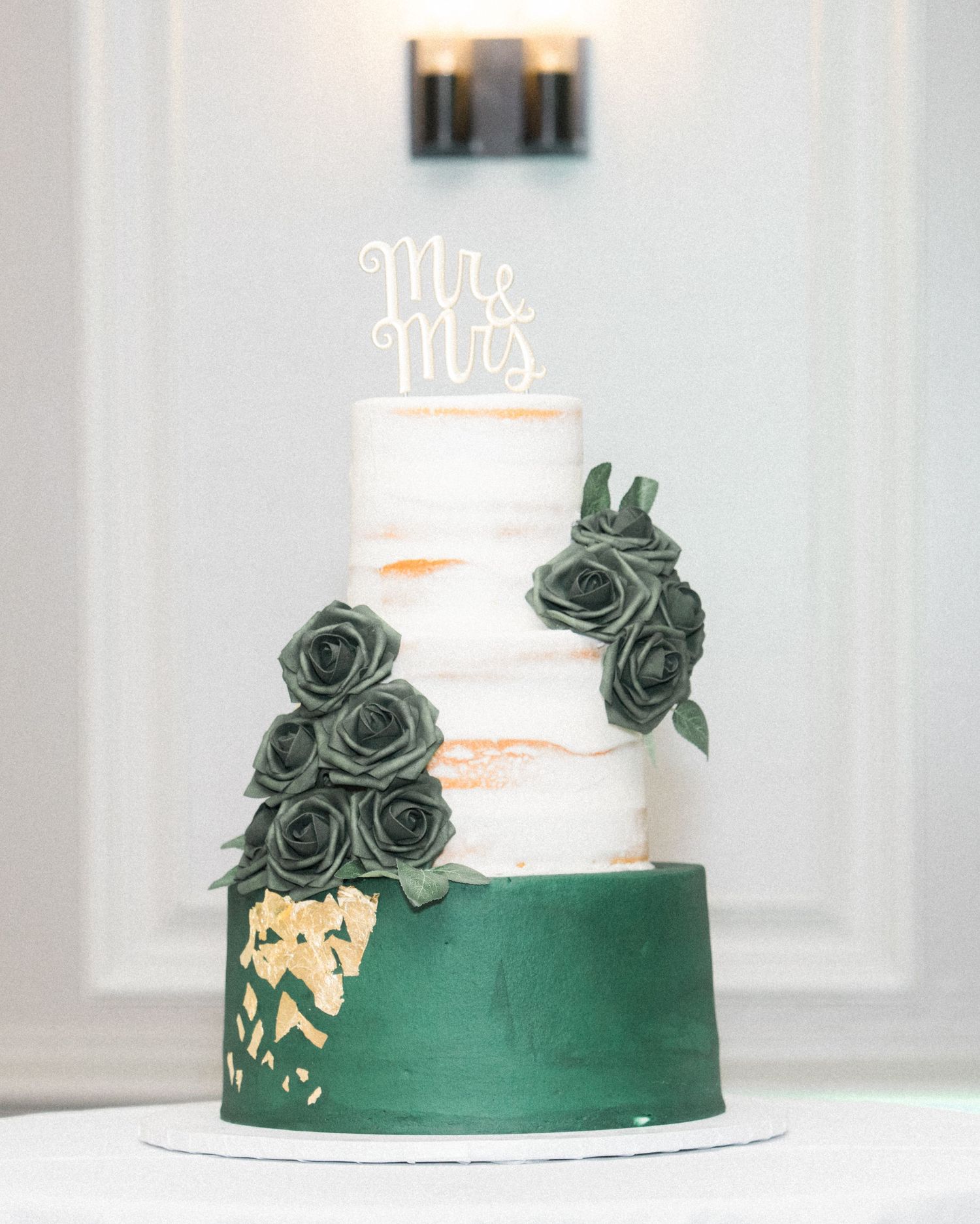 Elegant wedding cake decorated with dark green roses and gold accents.