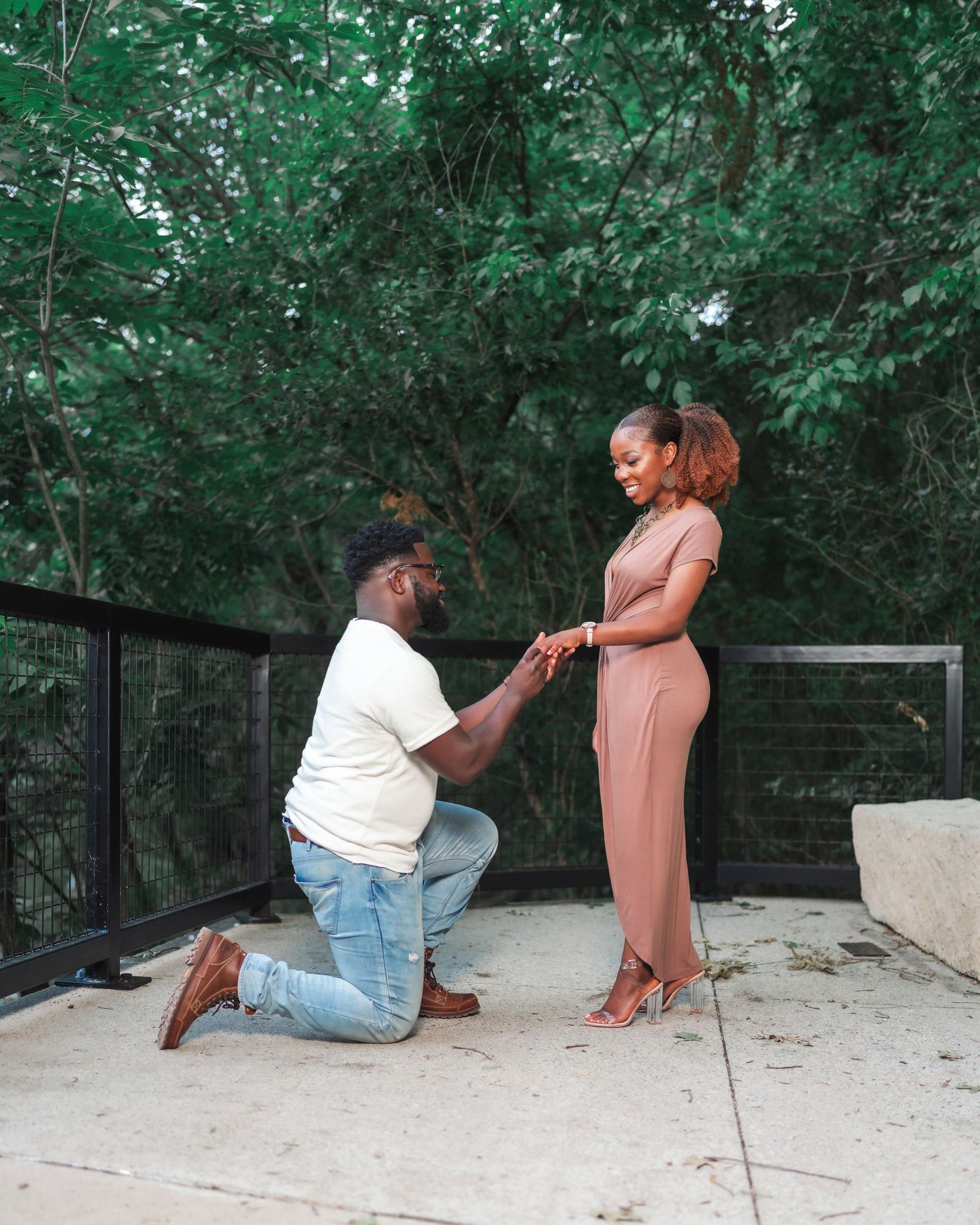 A couple engages in a tender moment on outdoor stone steps during what appears to be a proposal.
