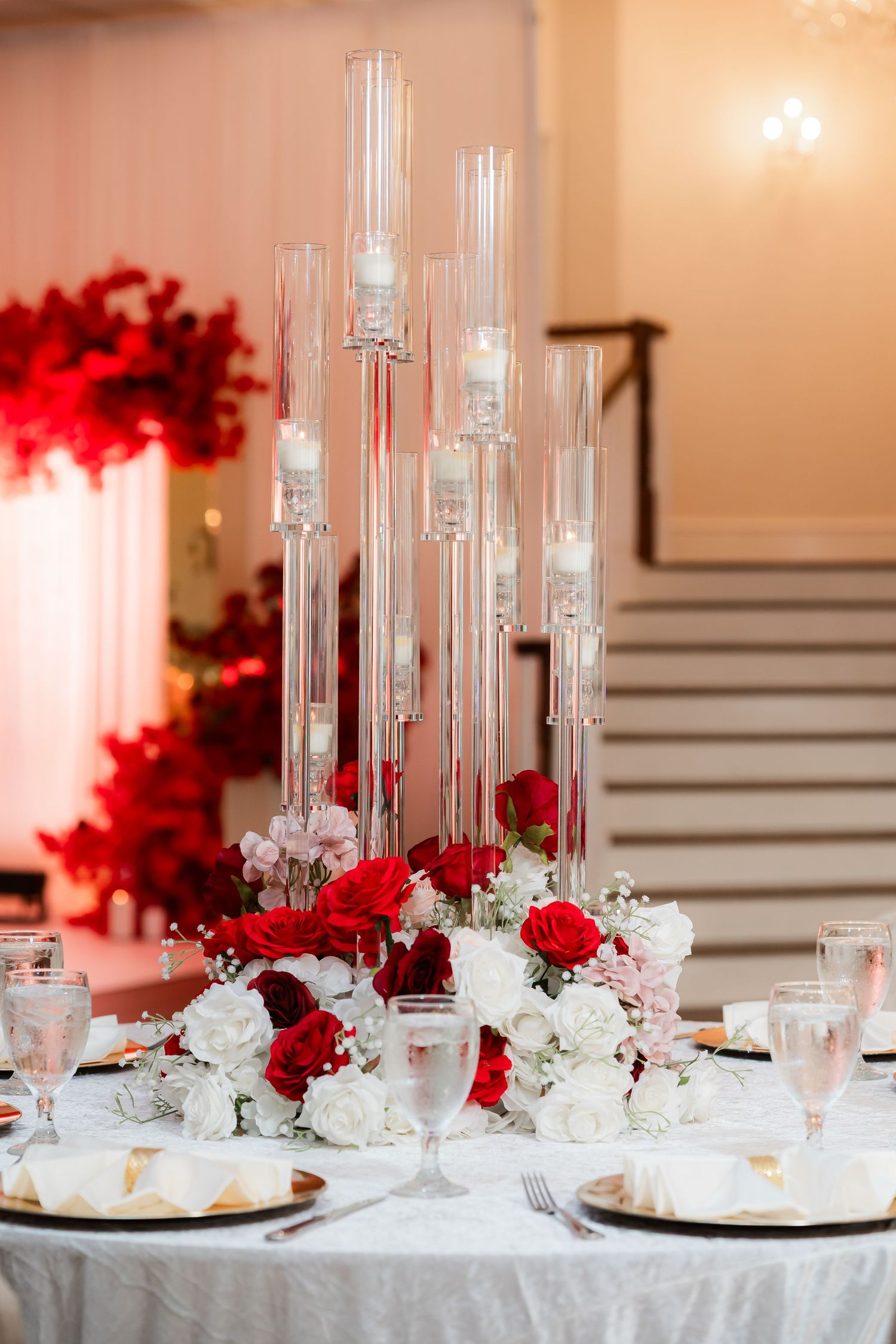 Formal table settings with tall glass centerpieces featuring red and white roses at a wedding reception.