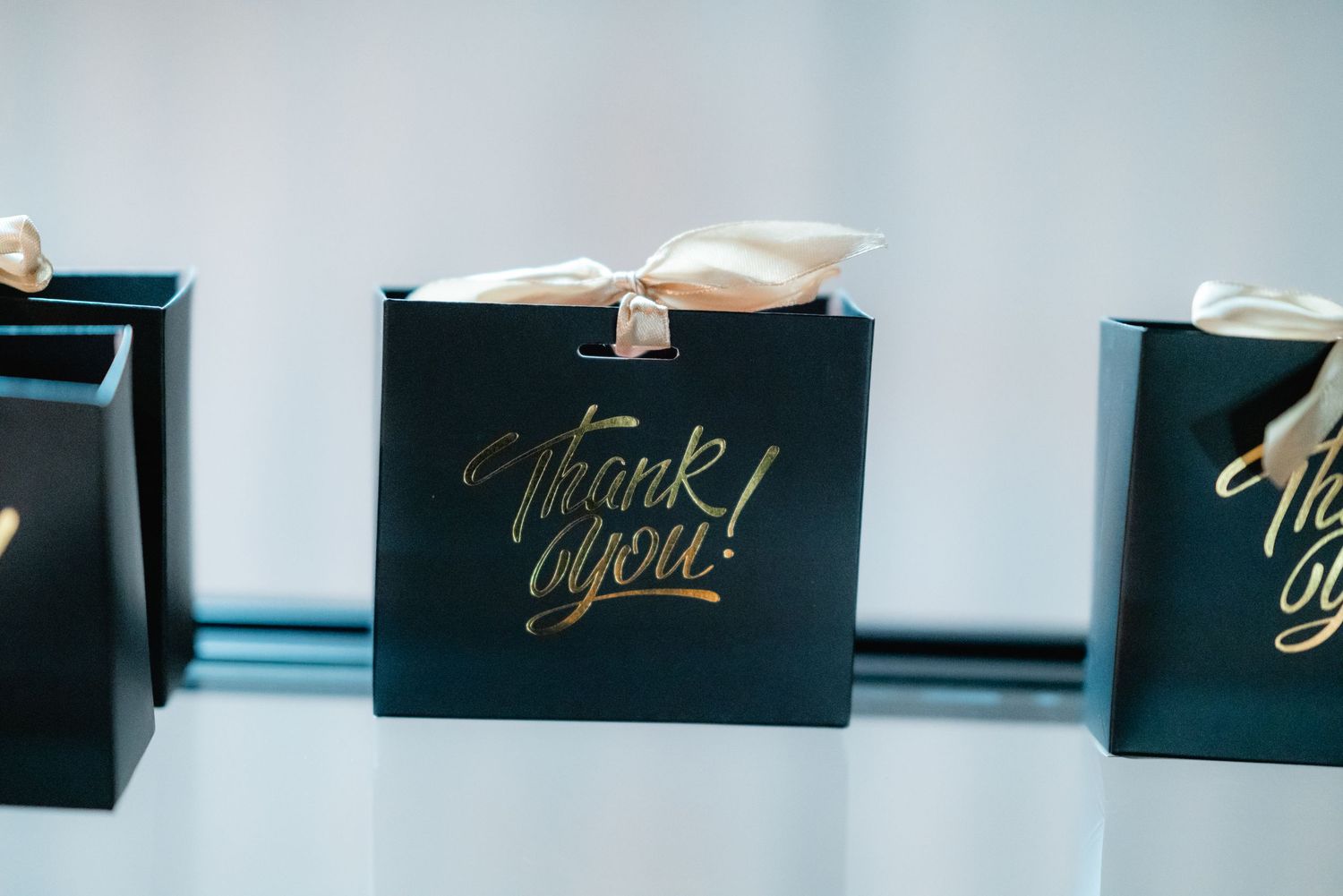 Elegant black gift boxes with gold lettering arranged in a row against light blue background.