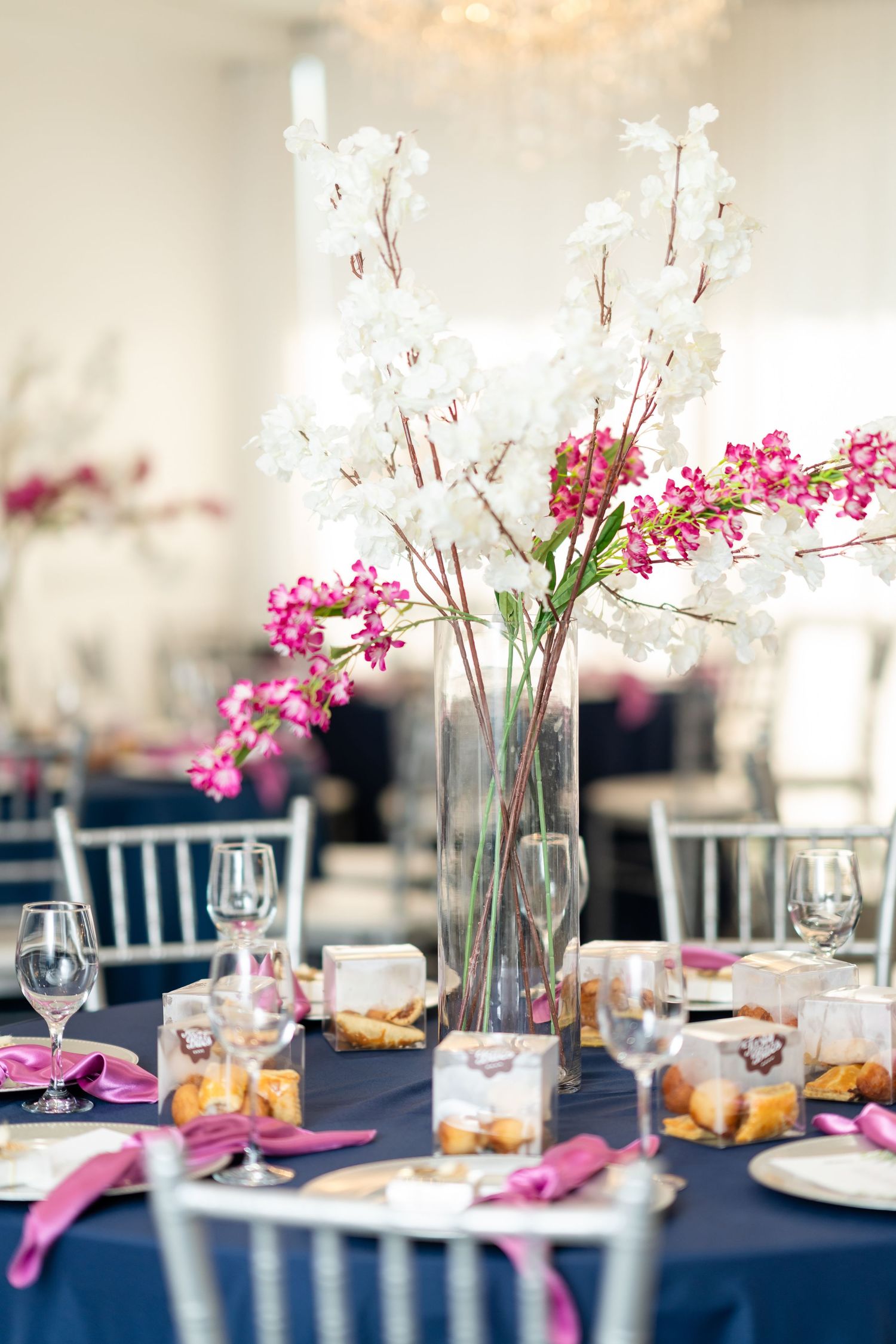 Elegant wedding reception table settings with navy linens, pink floral centerpieces, and wine glasses create a romantic atmosphere.