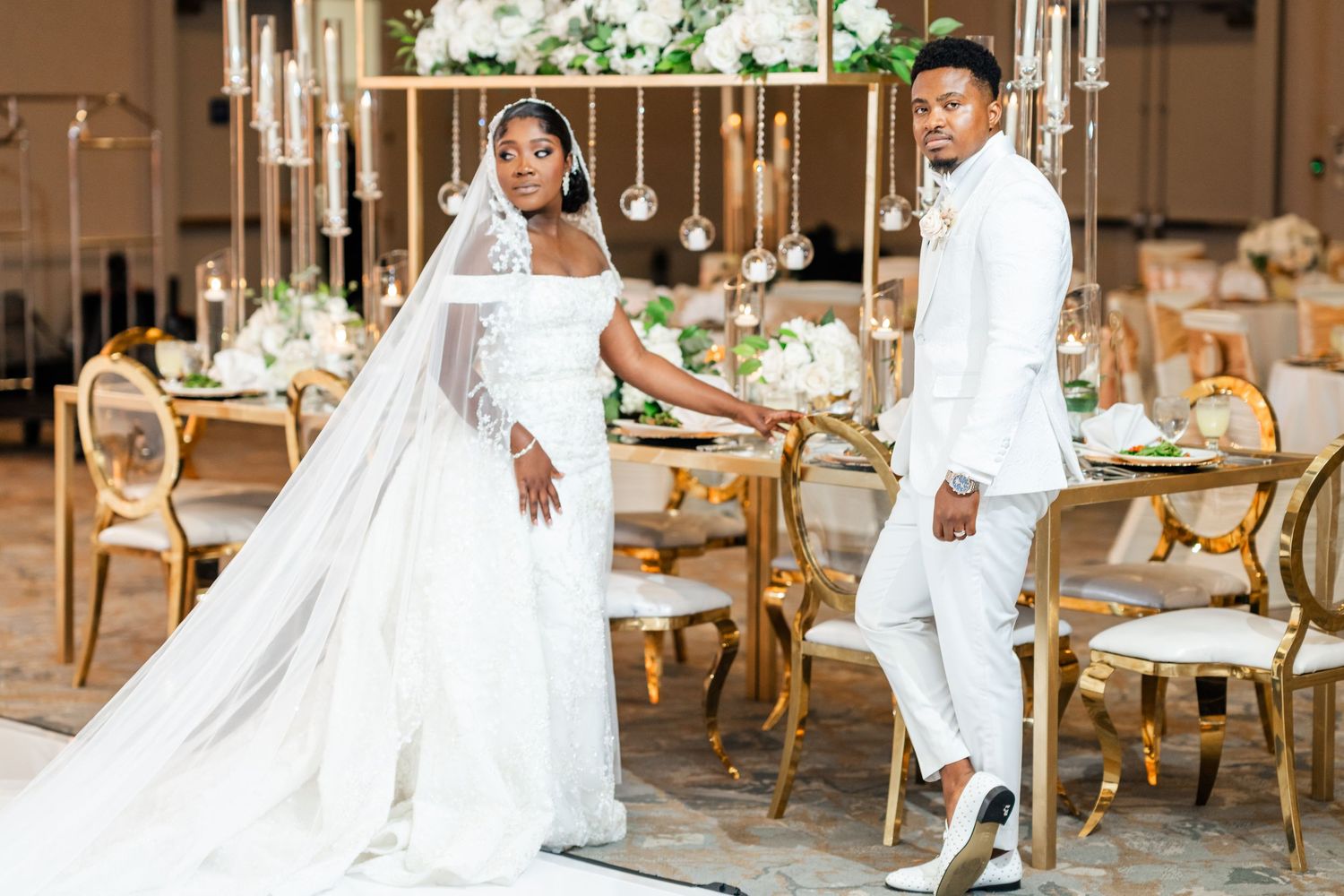Elegant wedding party dressed in white poses in a luxurious indoor venue with ornate furniture and decor.