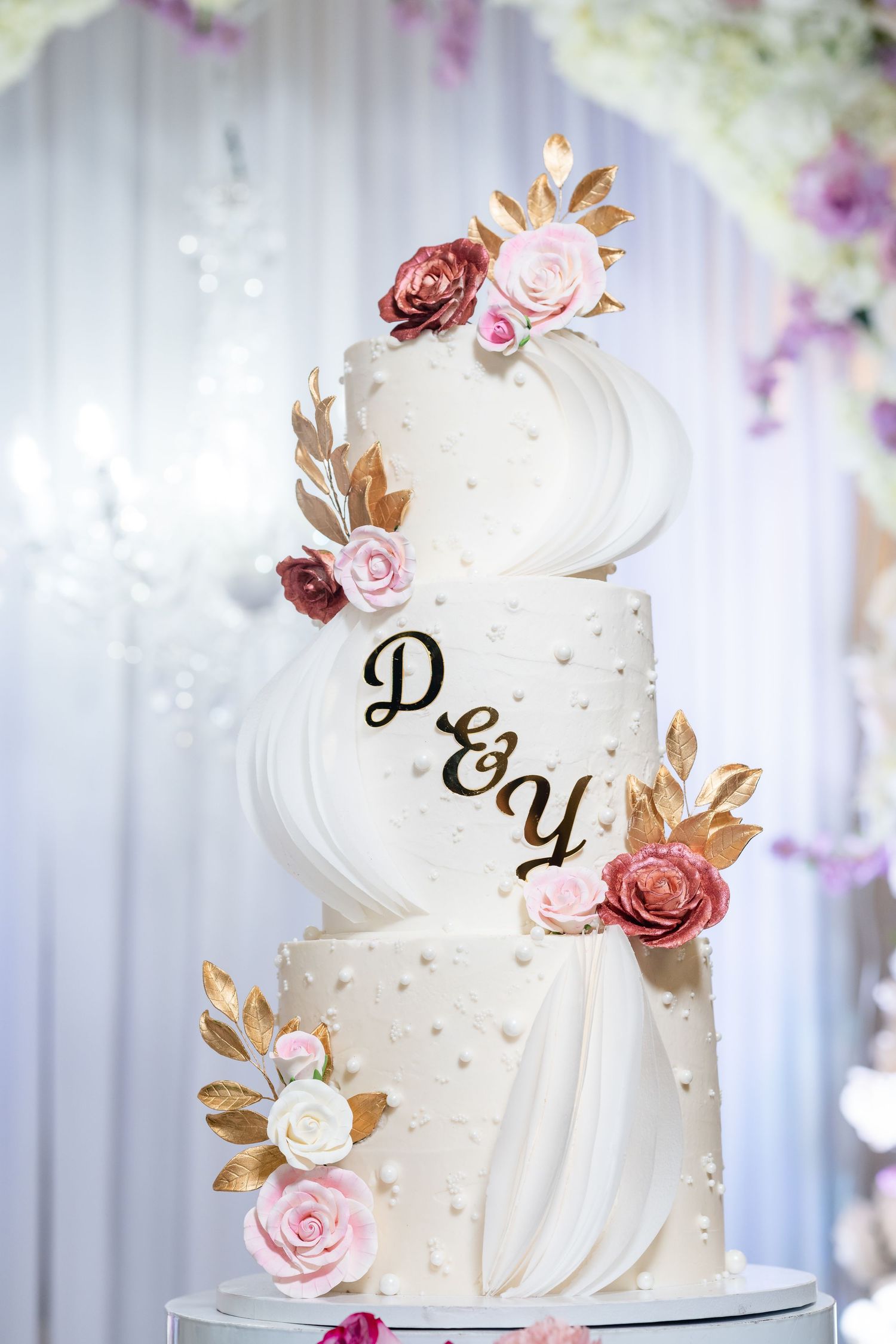 Elegant white wedding cake decorated with pink and gold floral accents and monogram details.