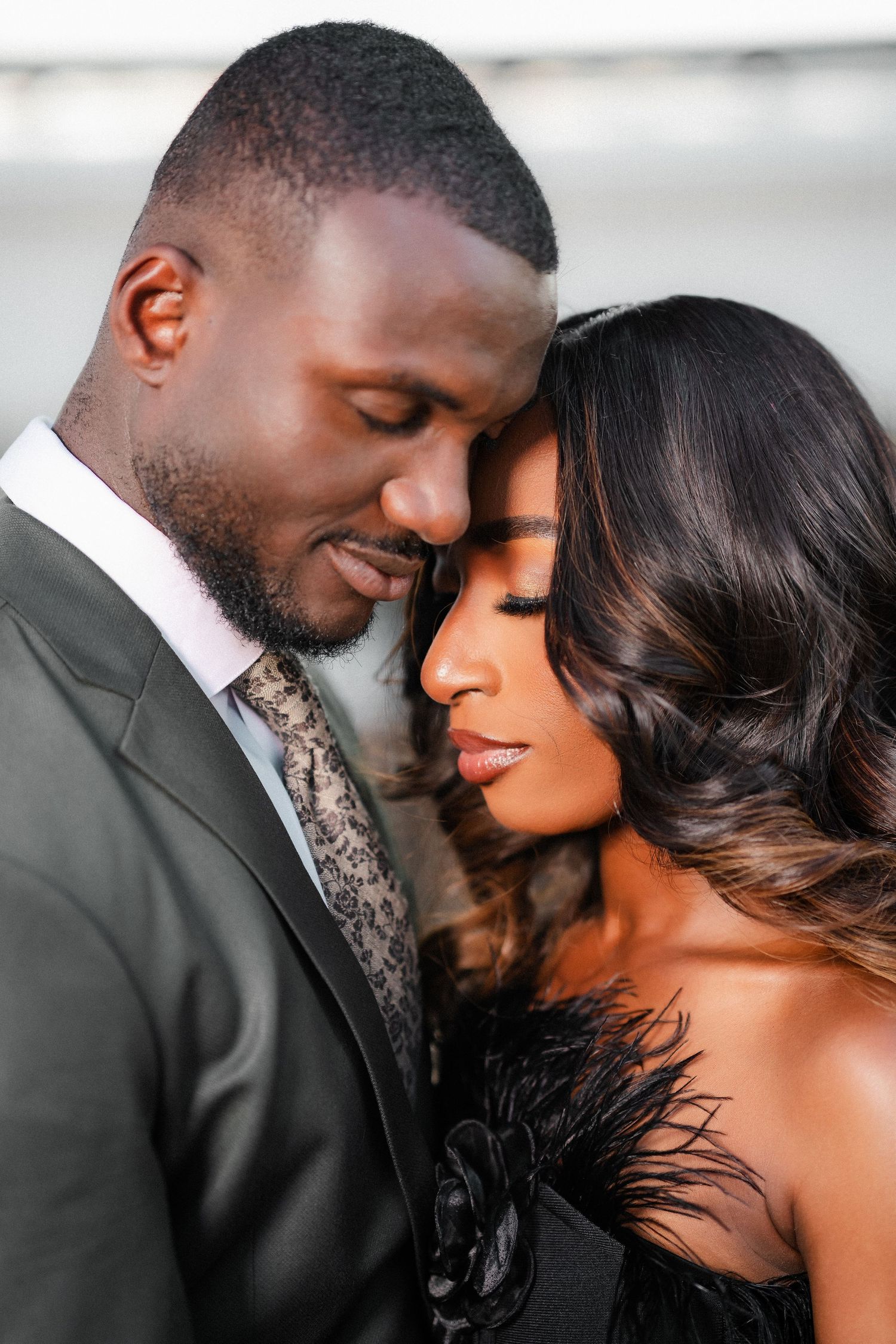 A romantic couple shares an intimate moment in formal attire during what appears to be an engagement or wedding photo shoot.