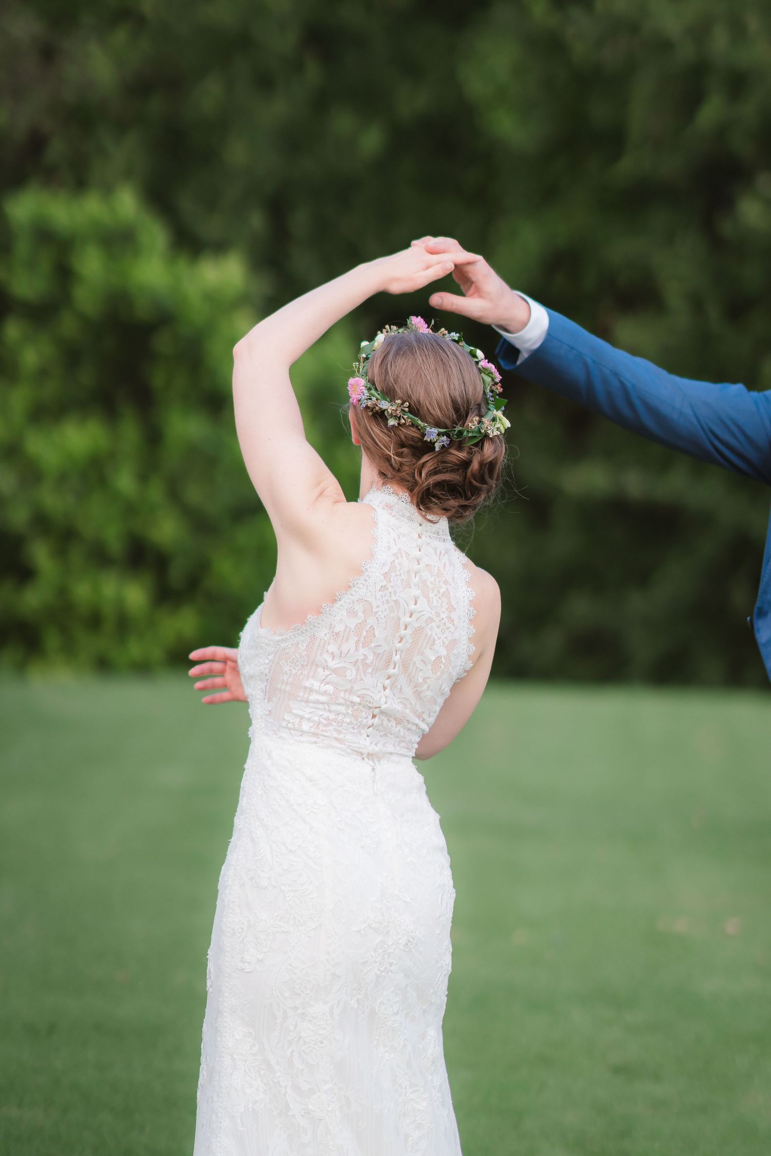 A bride in a white lace dress poses outdoors against a green natural background.