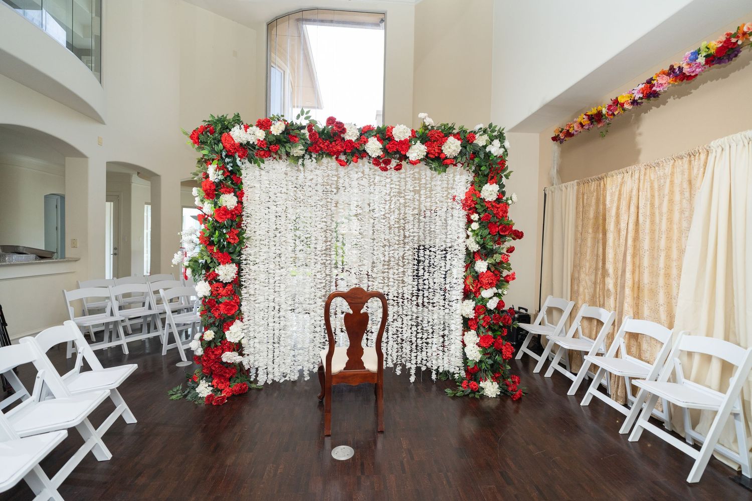Indoor wedding venue decorated with red floral arrangements and white chairs set up for a ceremony.