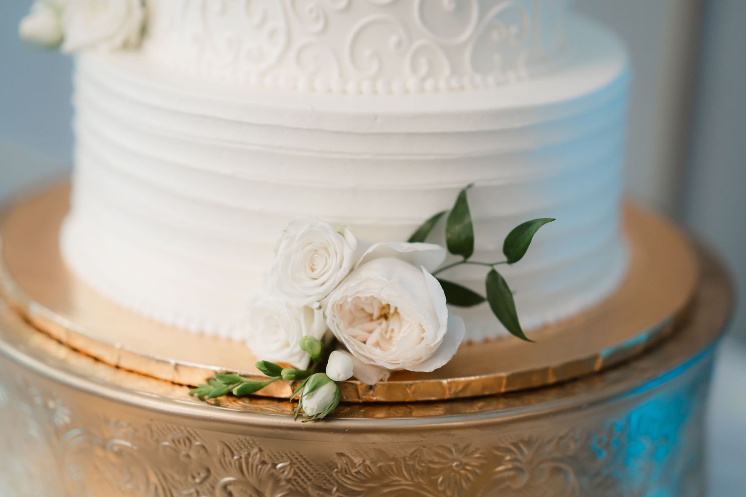 Classic white tiered wedding cake with intricate piping and fresh floral accents.