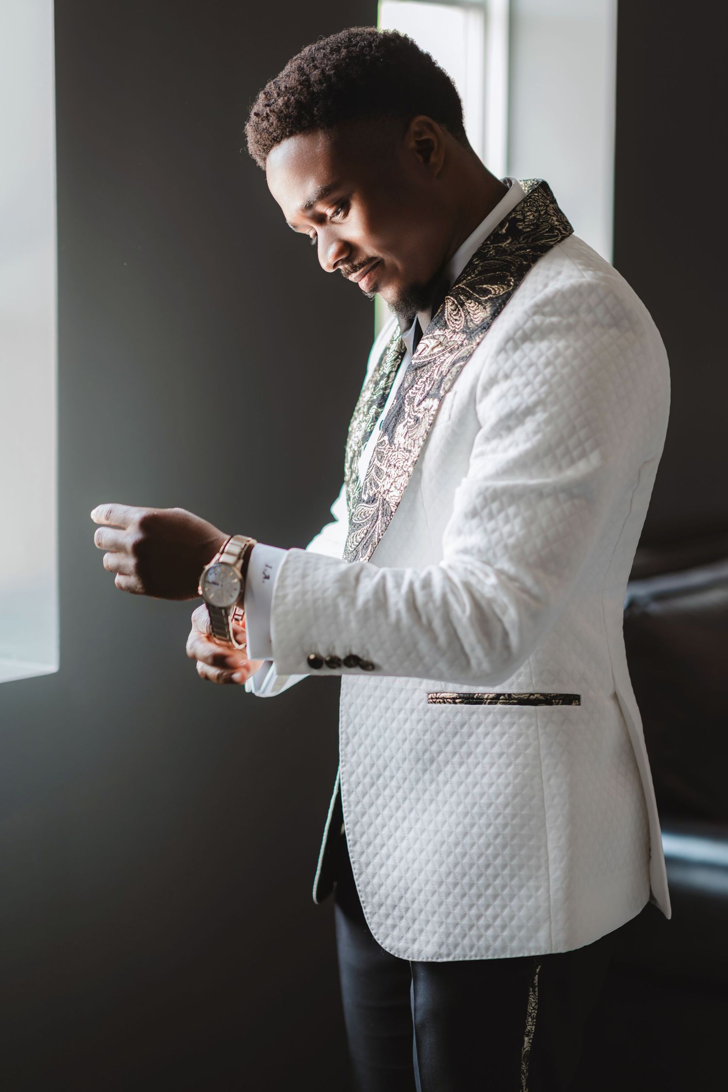 A person in a white textured vest adjusts their bowtie while getting ready for a formal event.