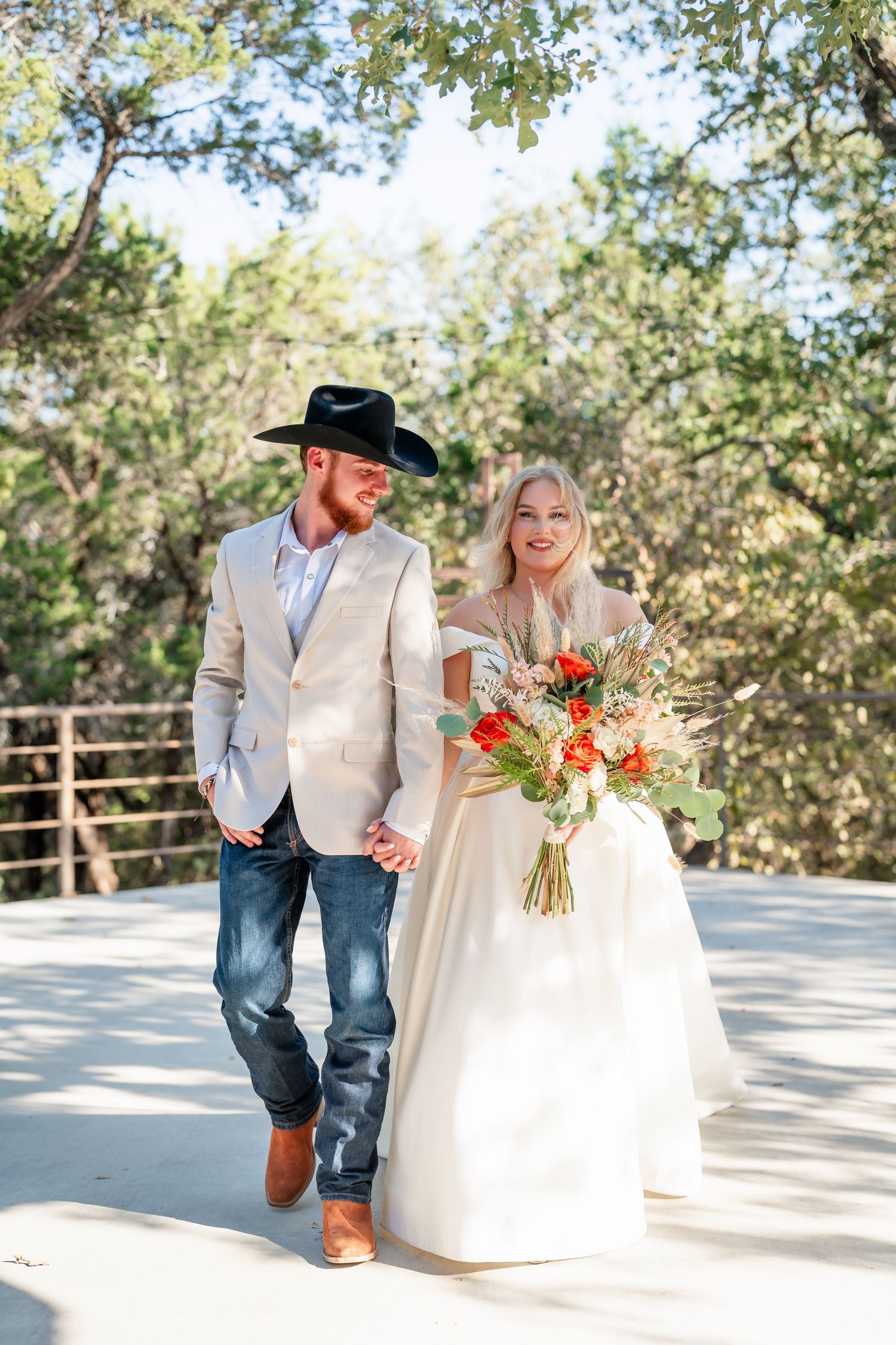 Joyful wedding couple walking together on outdoor deck with orange floral bouquet.