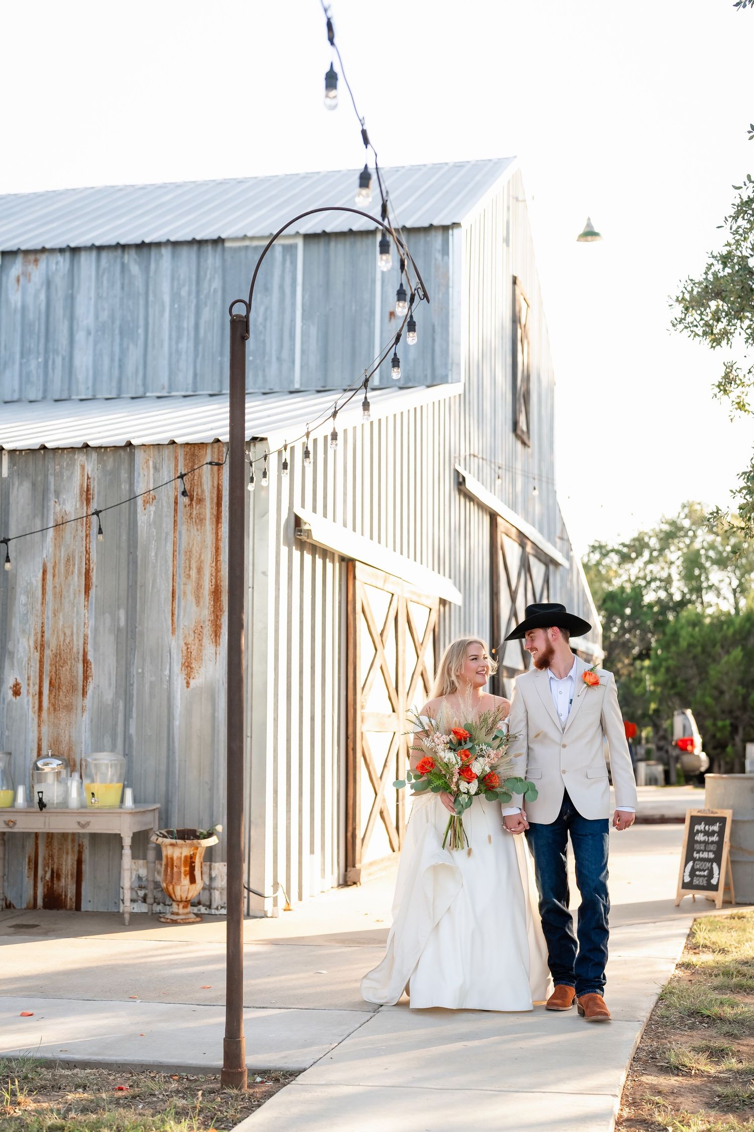 Wedding couple poses outside rustic metal barn with string lights.