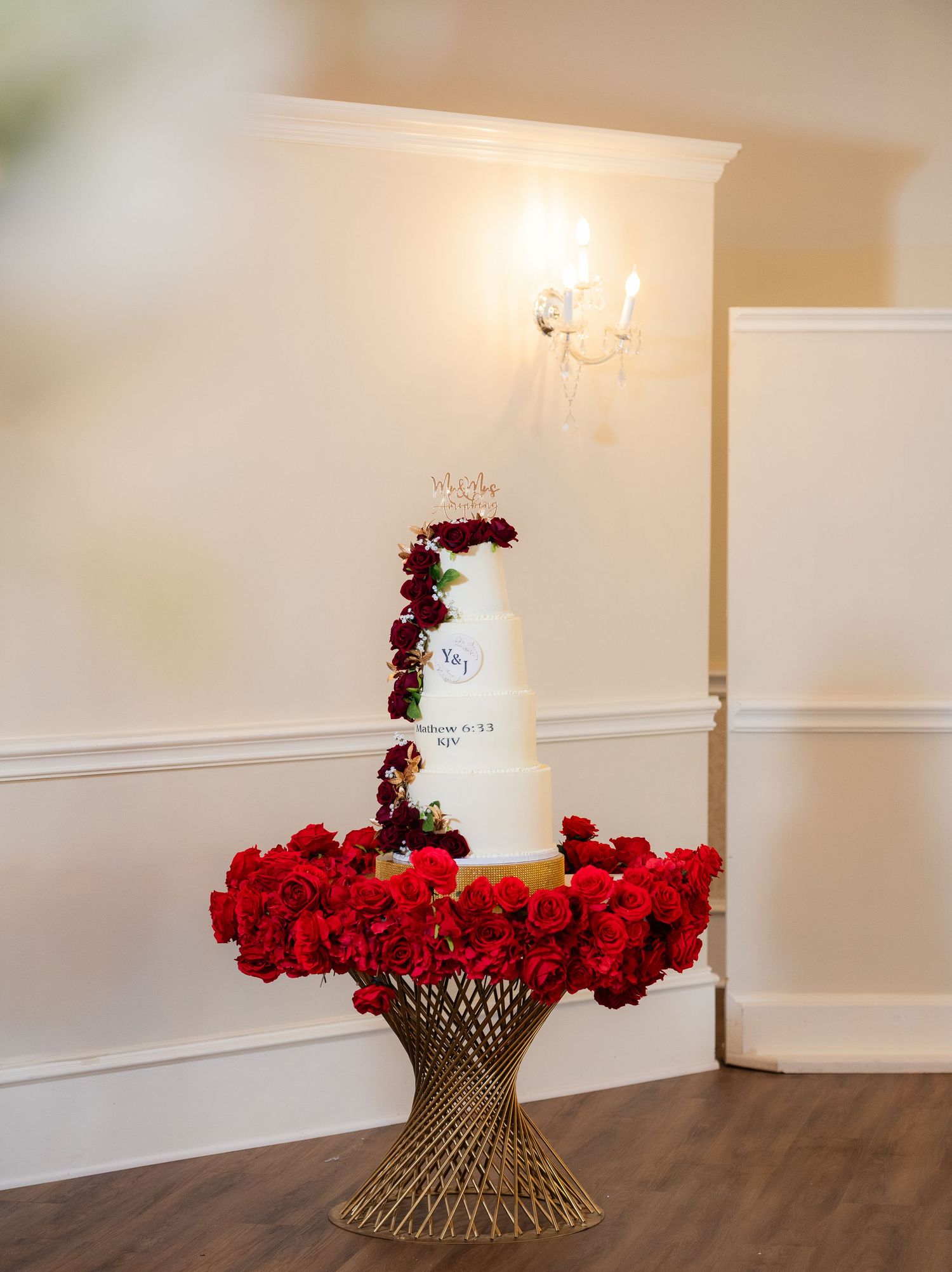 Elegant floral arrangement featuring bright red roses on a metallic pedestal stand against a white wall.
