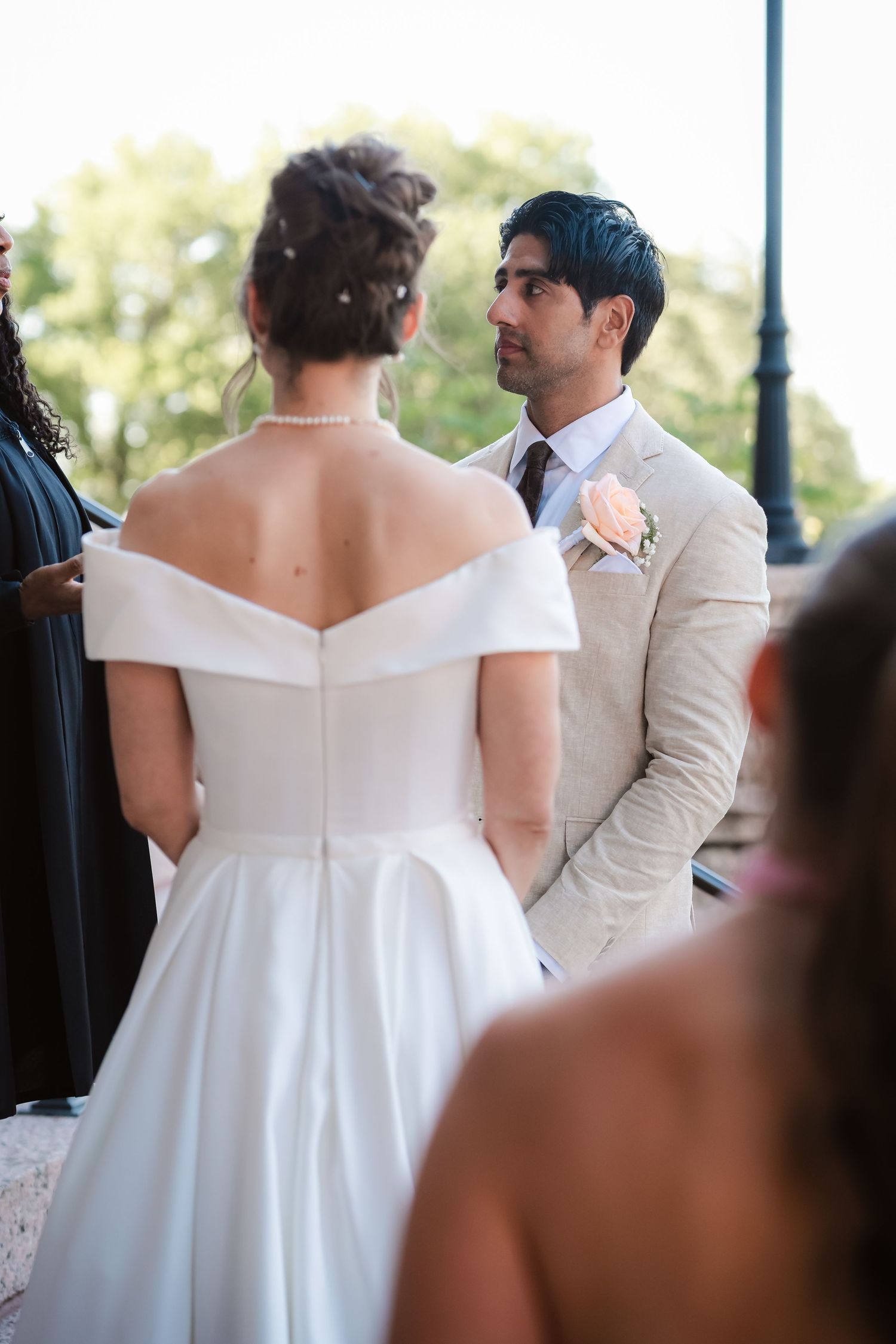 Wedding couple in white dress and beige suit photographed from behind during ceremony.