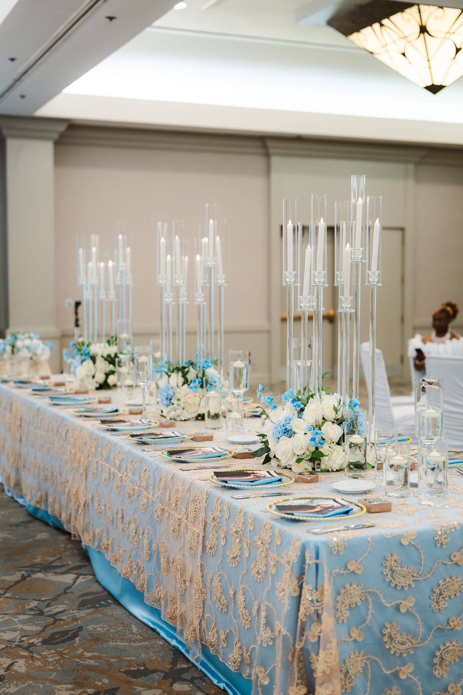 Elegant wedding reception table setup with light blue linens and tall glass centerpieces.
