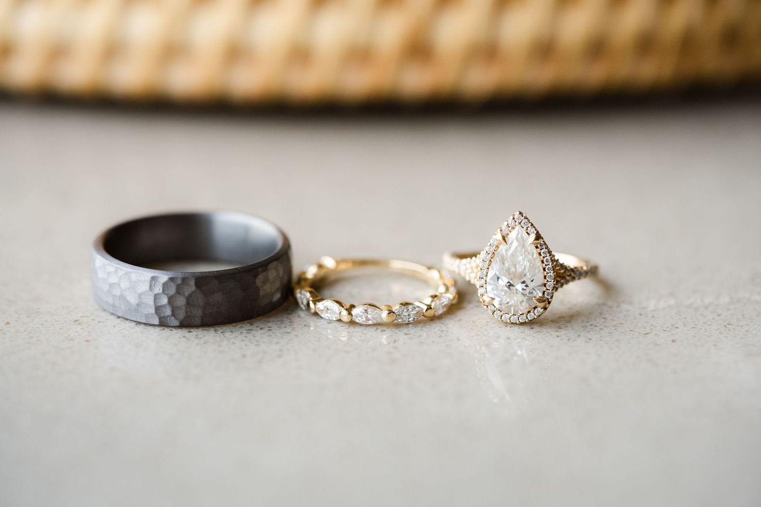 Close-up of delicate wedding rings and jewelry displayed on a neutral textured surface.