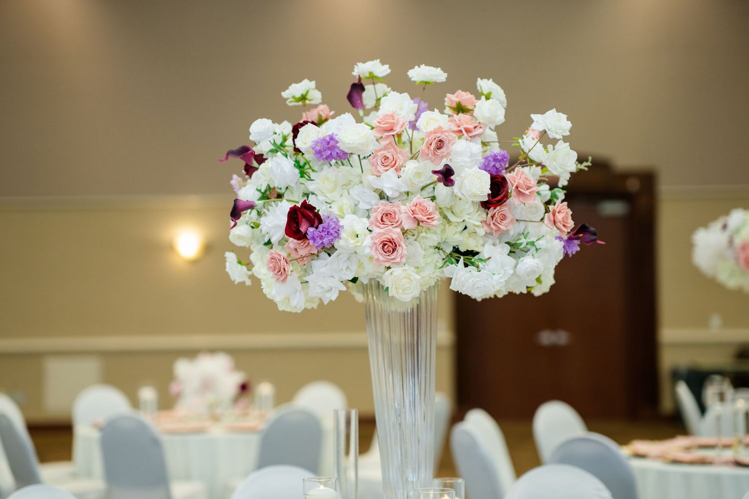 Elegant wedding reception centerpieces with white floral arrangements in tall silver vases.