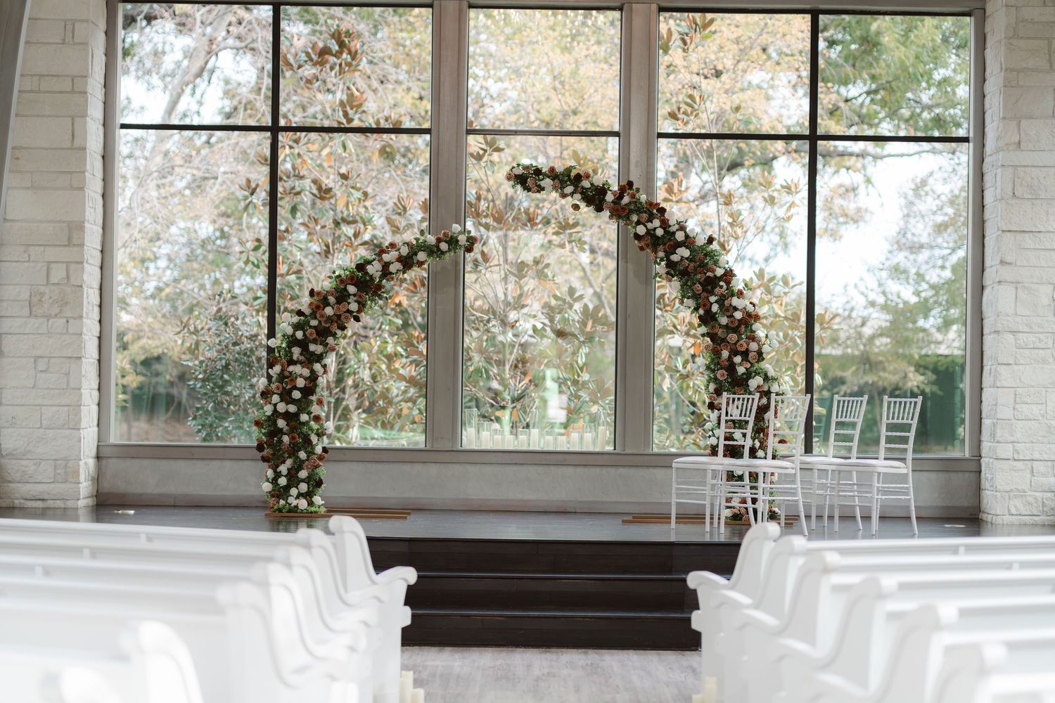 Light-filled chapel venue with large windows and floral arch for wedding ceremony.