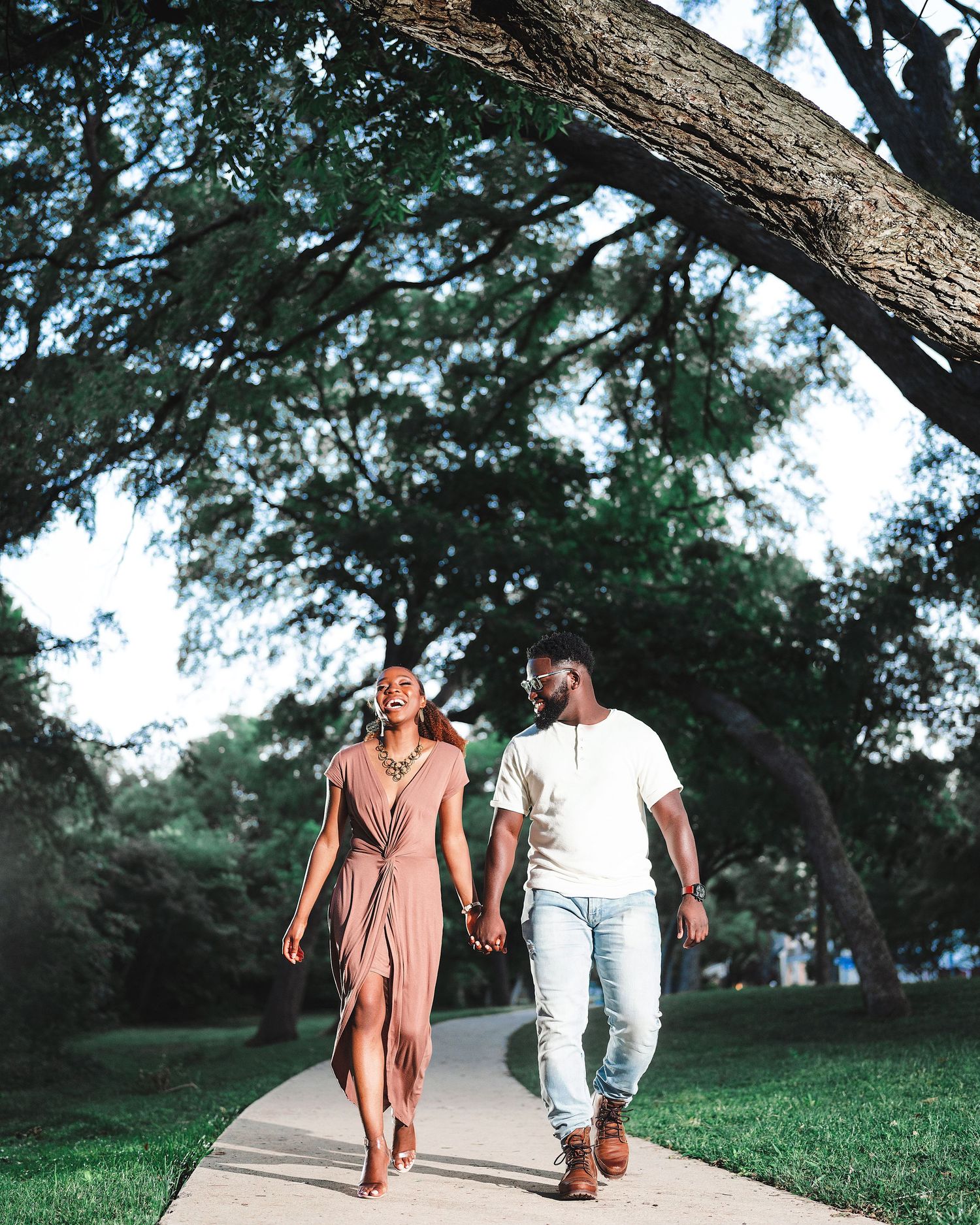 A couple walks along a tree-lined path during a summer photoshoot.