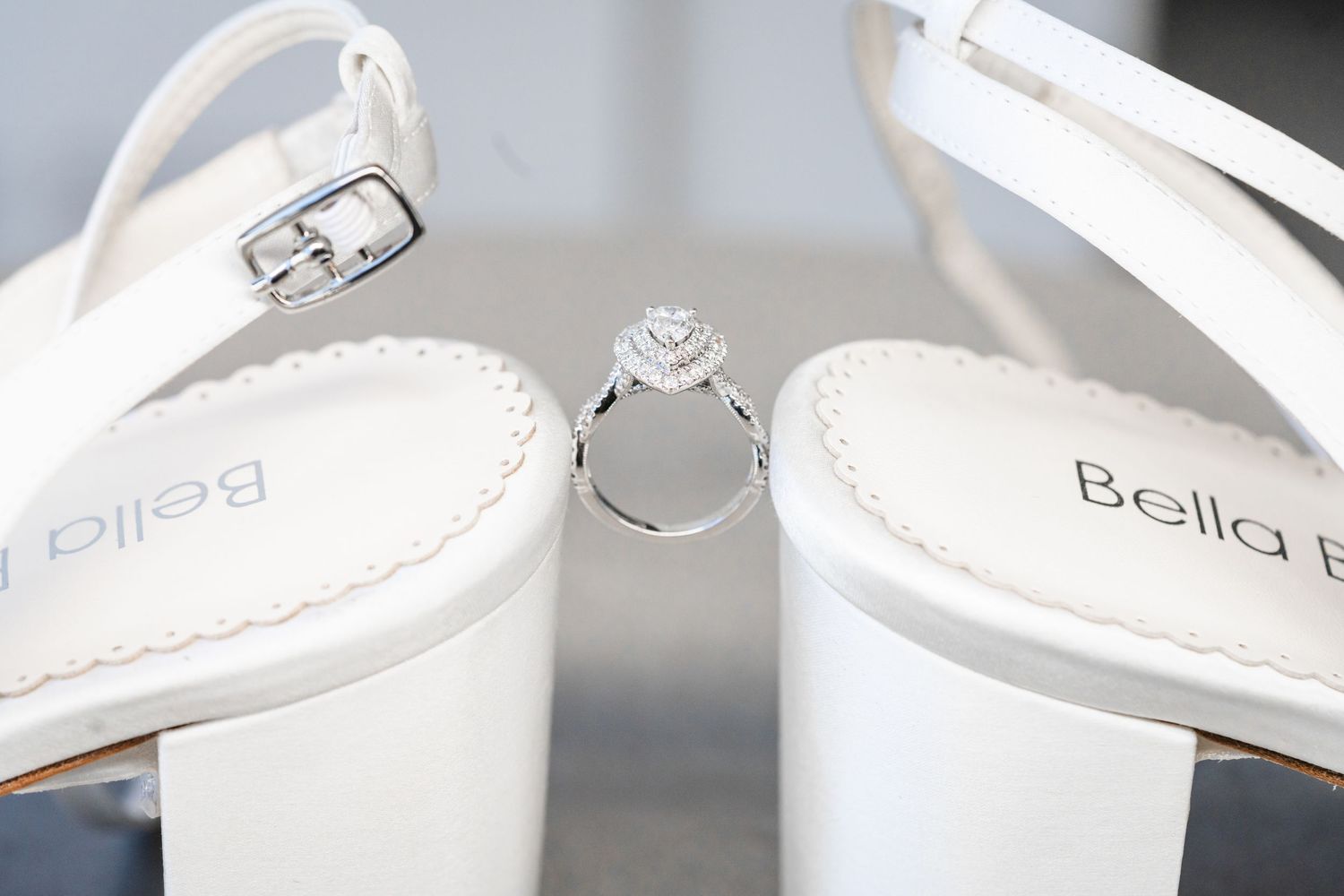 Diamond engagement ring nestled between white bridal heels with crystal embellishments.