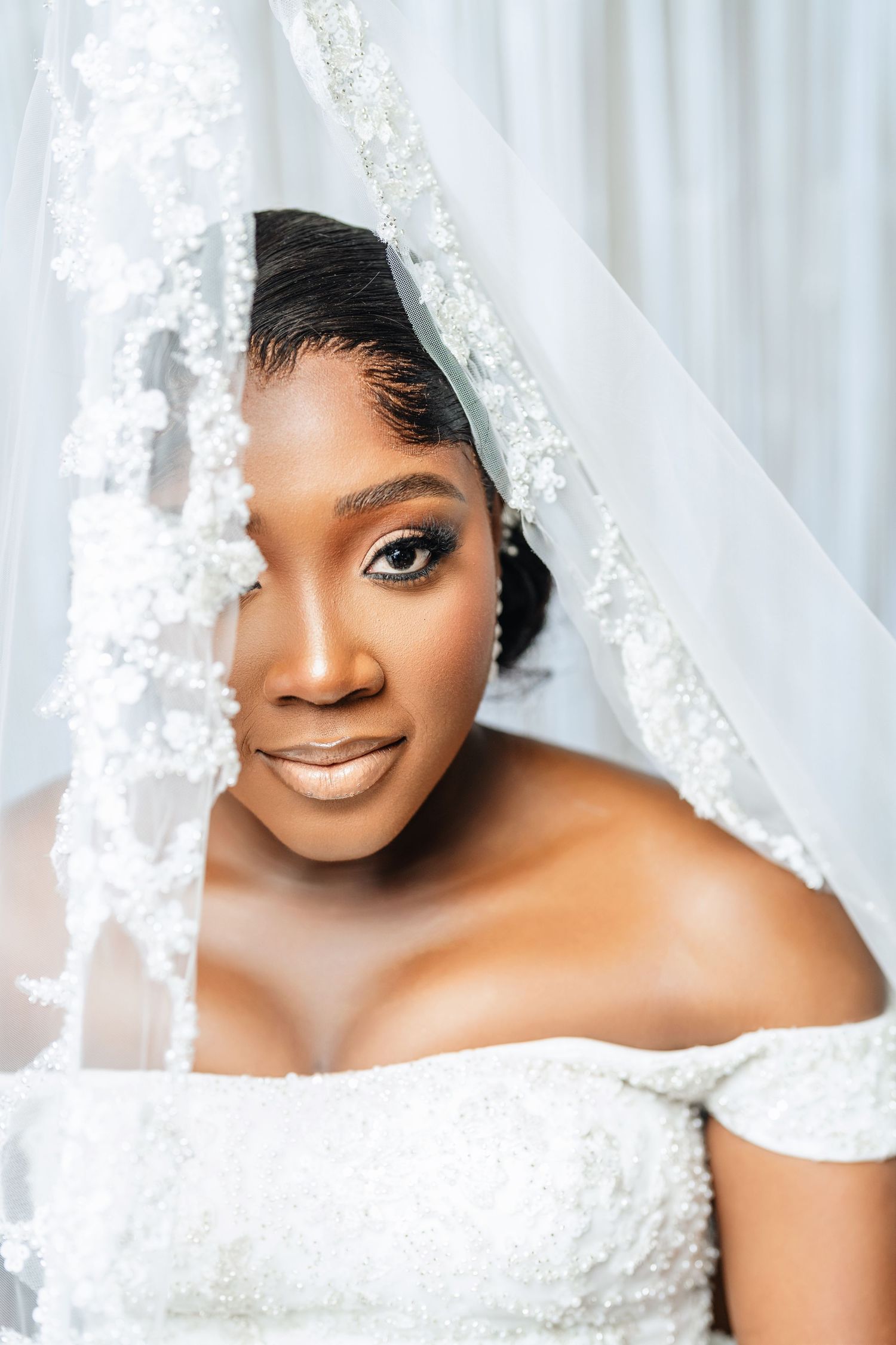 Bridal portrait through delicate lace veil against white background.