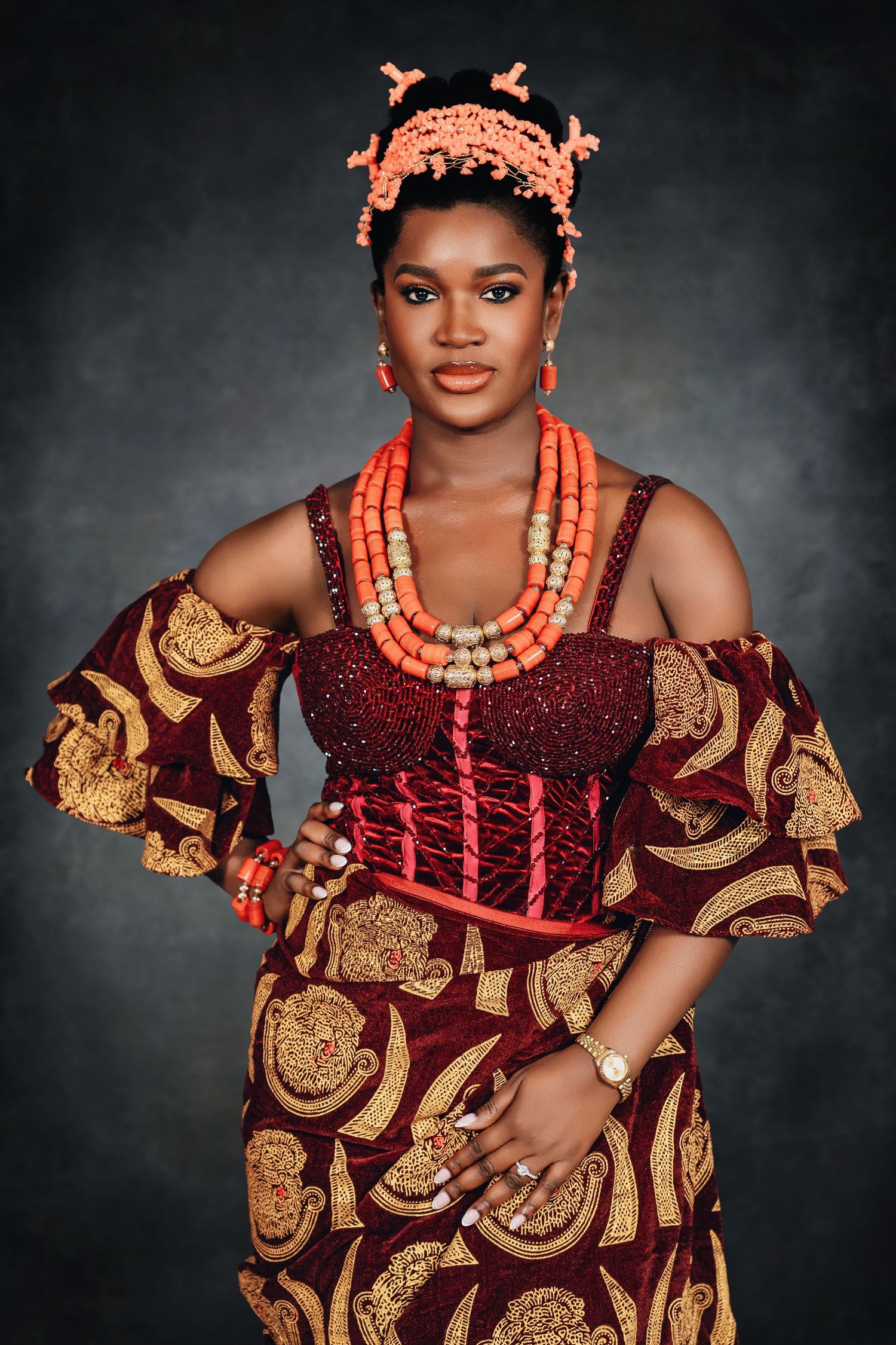 Traditional African bridal portrait featuring ornate coral beads, burgundy and gold ankara fabric, and detailed headpiece.
