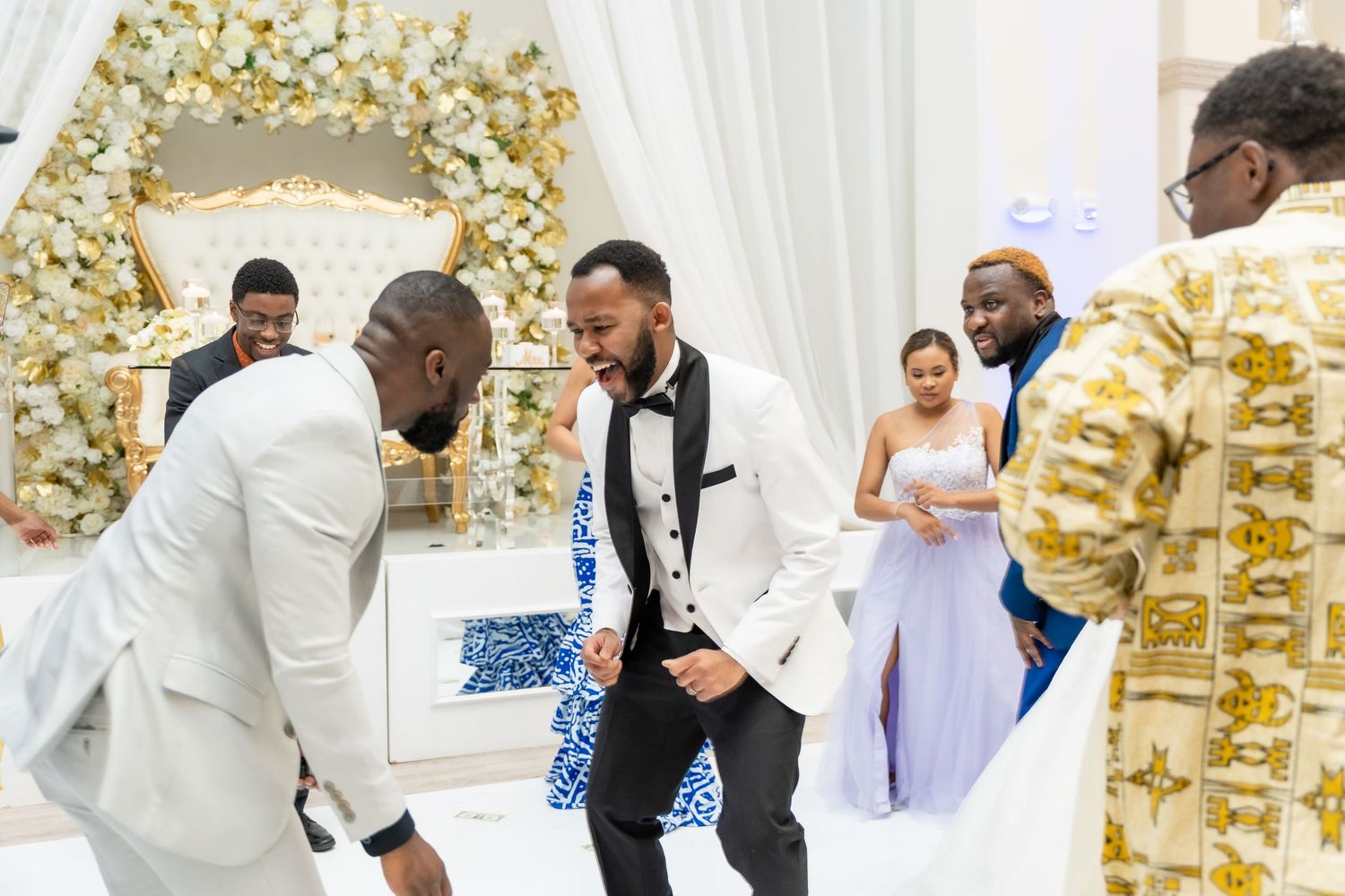 Wedding guests celebrate around an elegant gold and white decorated reception table.