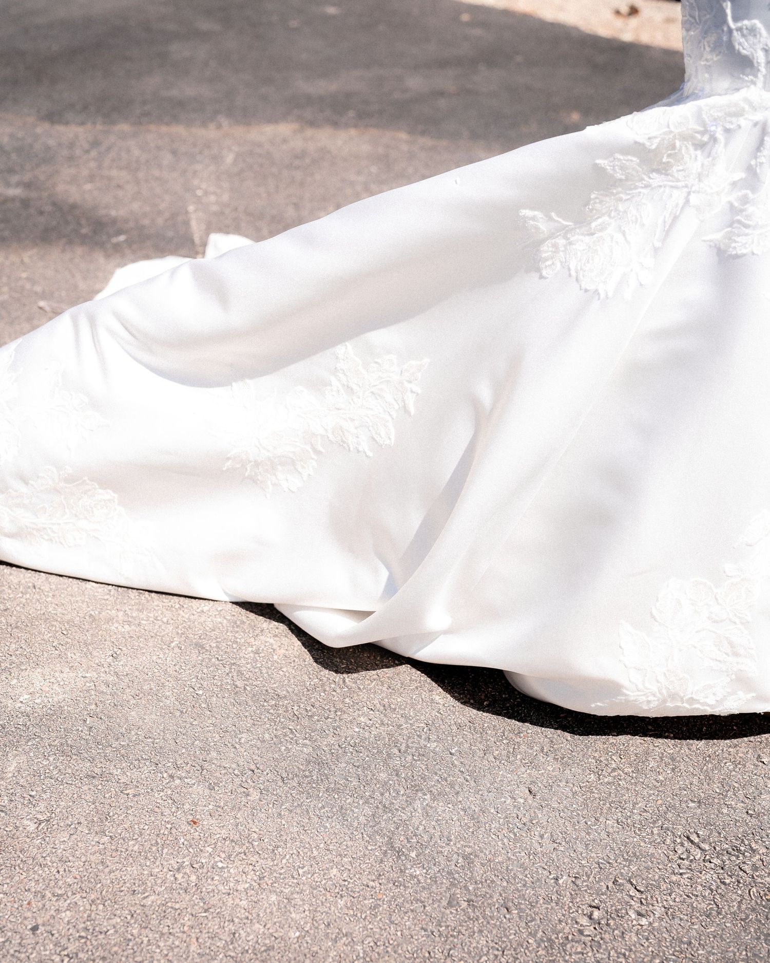 Long flowing white wedding dress train dragging elegantly across concrete ground in multiple angles.