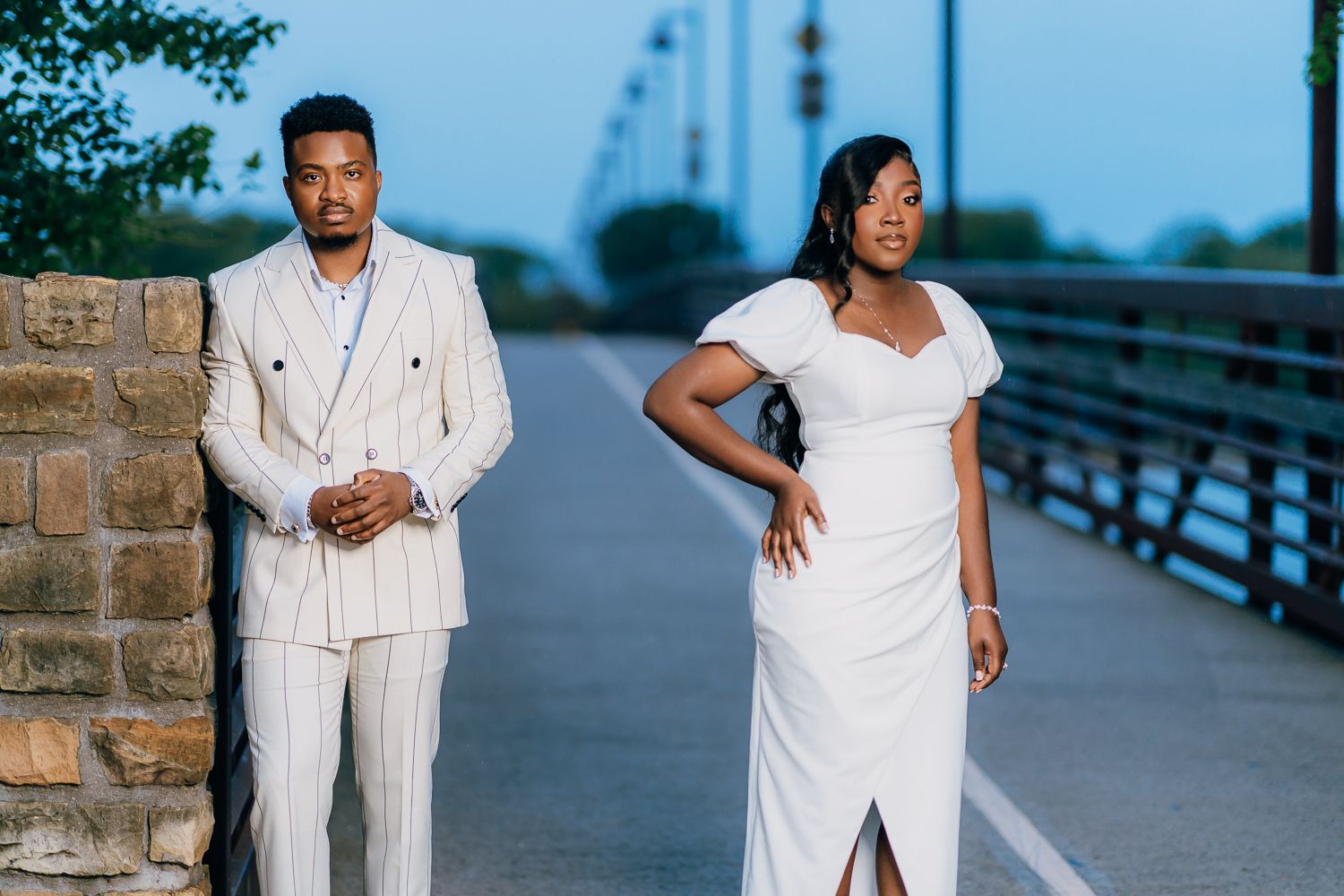 A group of people in white outfits pose along a waterfront boardwalk at dusk.