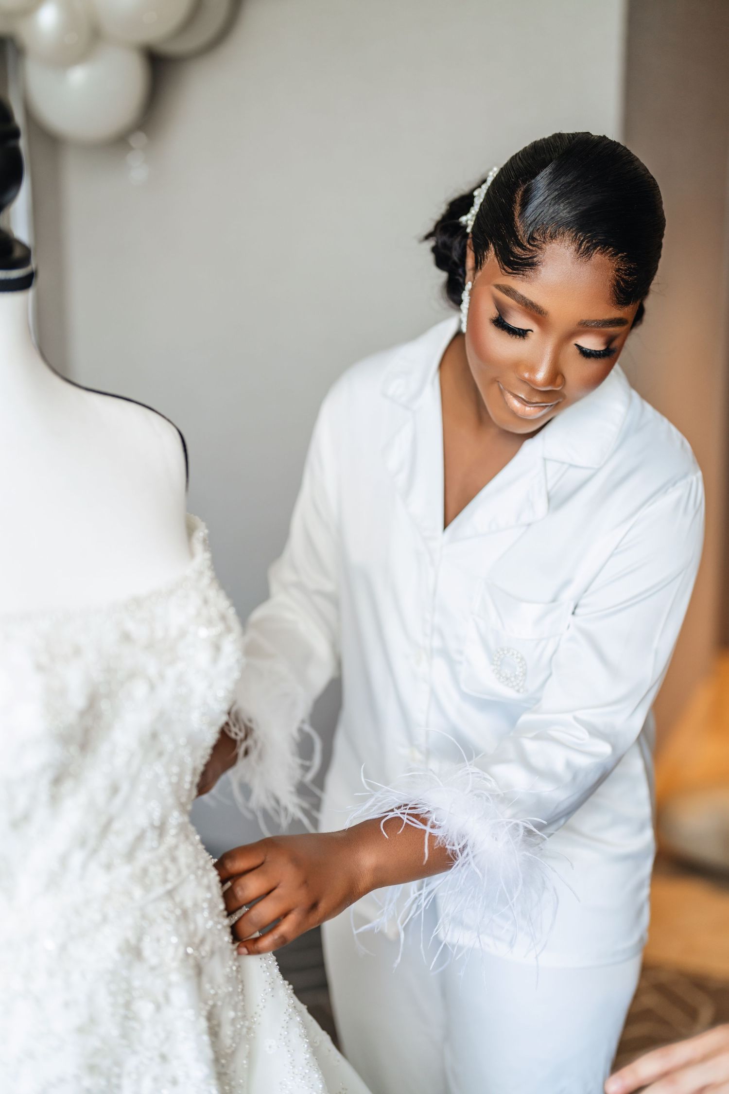 A person in a white robe carefully examines a textured white wedding dress displayed on a mannequin.