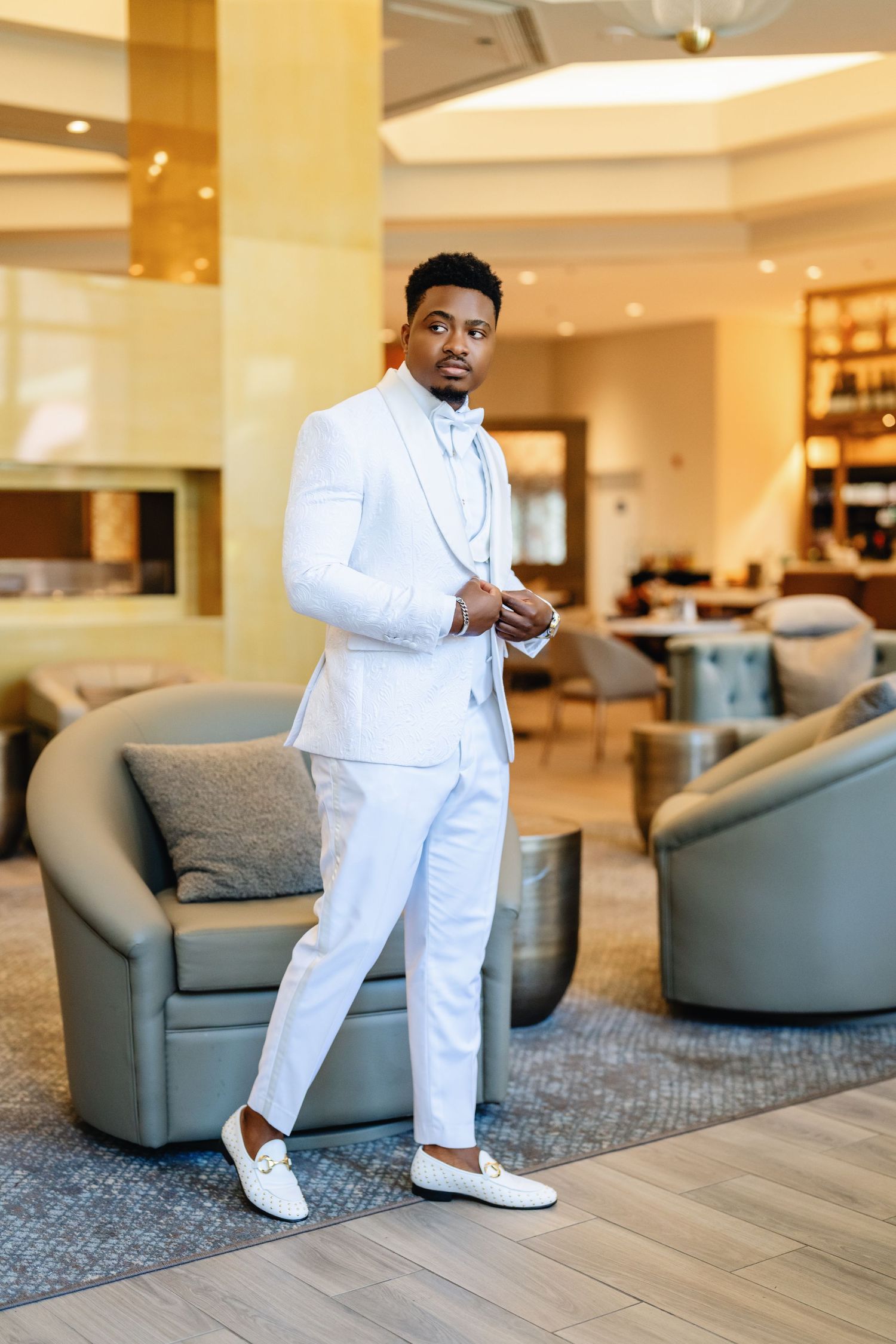 Stylish all-white suit ensemble paired with white loafers in an elegant hotel lobby setting.
