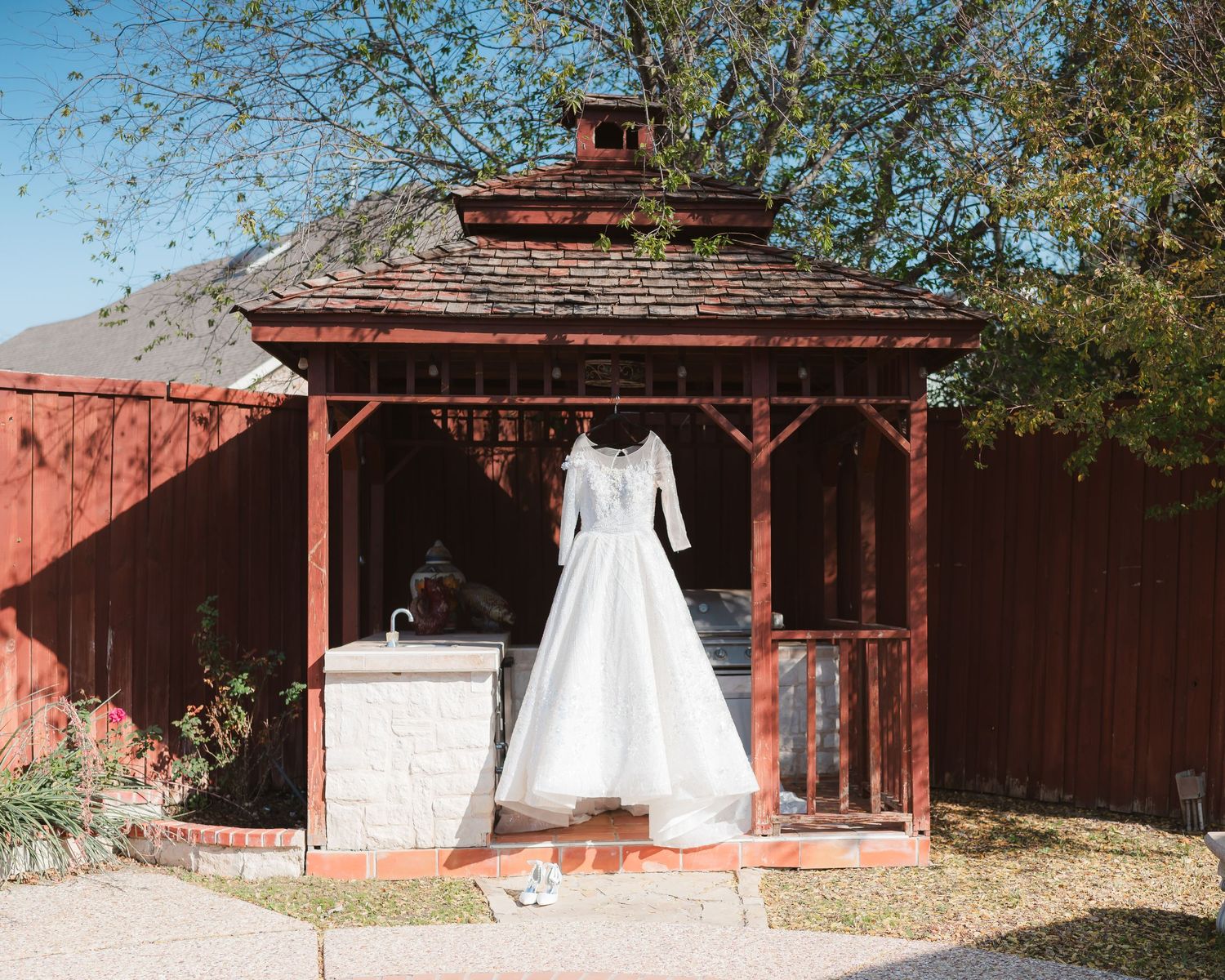 Classic white wedding dress displayed in rustic wooden gazebo against red barn.