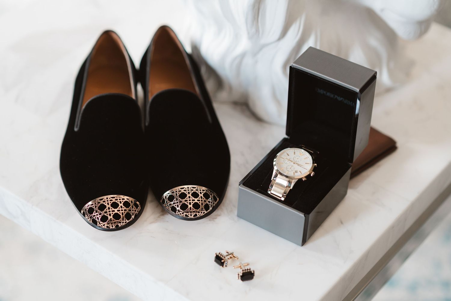Wedding accessories including elegant black shoes and jewelry arranged on white marble surface.