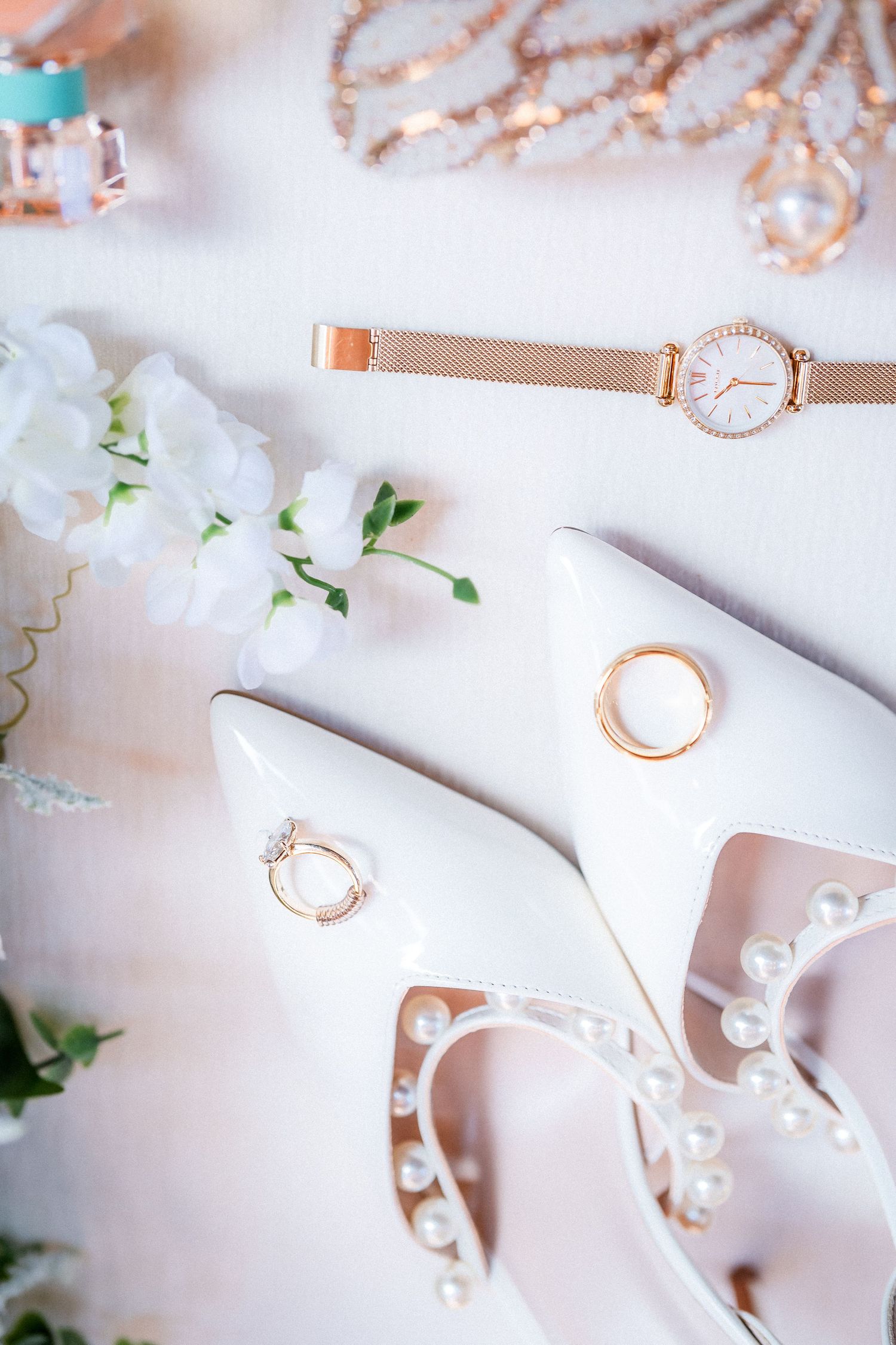 Delicate rose gold wedding accessories and jewelry arranged on white fabric.