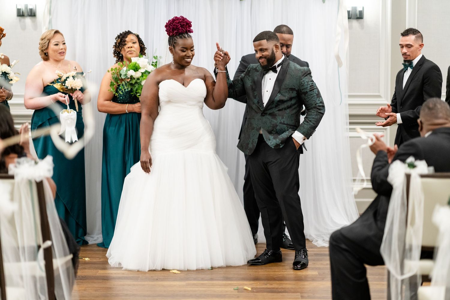 Wedding reception celebration with guests dancing and celebrating in elegant white venue.